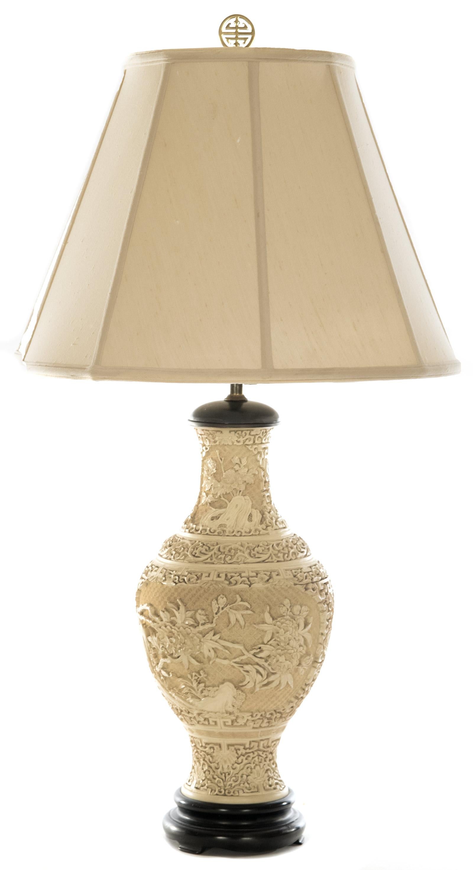 A 19th century hand-carved white Cinnabar table lamp of baluster form, topped with a cream shade and pierced gold finial, the body fitted between a wood neck cap and a stepped footed base. The body is covered all-over in high relief flowers and