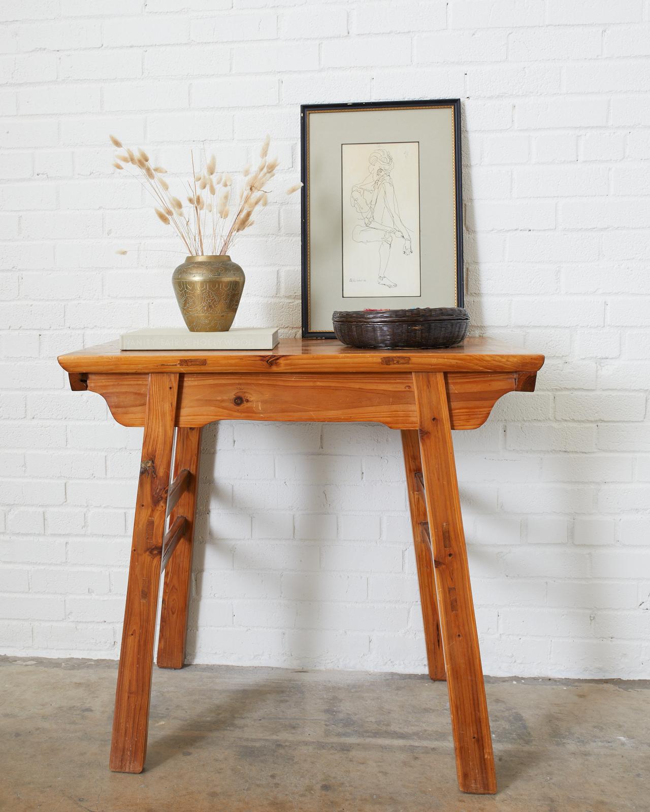 Chinese Ming style wooden wine table featuring a floating top panel and a simple carved apron and spandrels. Finished in a light natural clear lacquer. It has square legs and dual stretchers on each side of the splayed legs. Mortise and tenon