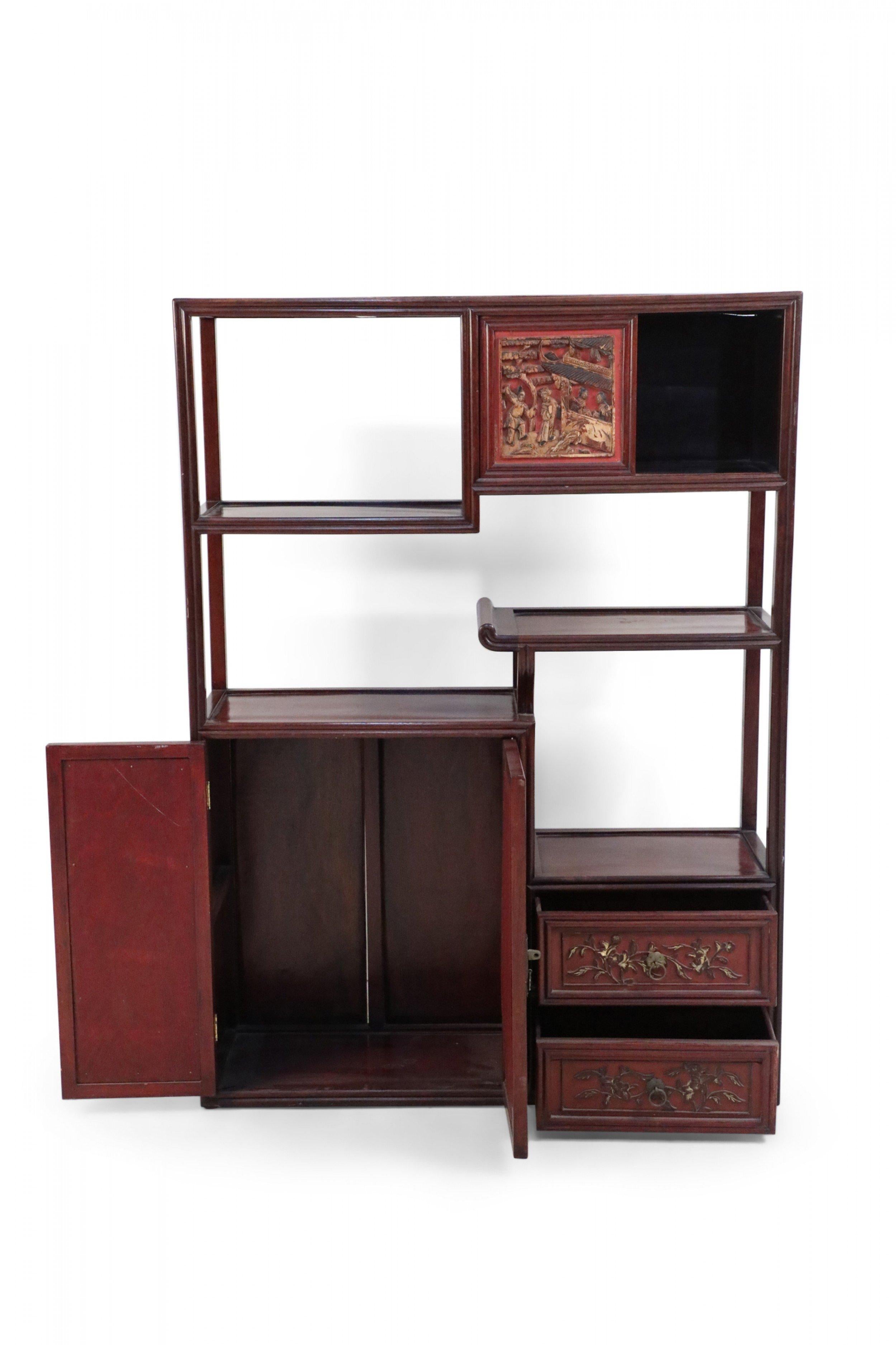 Chinese Bogu wooden etagere featuring open display shelving connecting ornately carved, red framed doors, two red drawers with golden foliage ornamentation and drawer pulls, and sliding doors, decorated in richly-depicted raised figurative scenes.