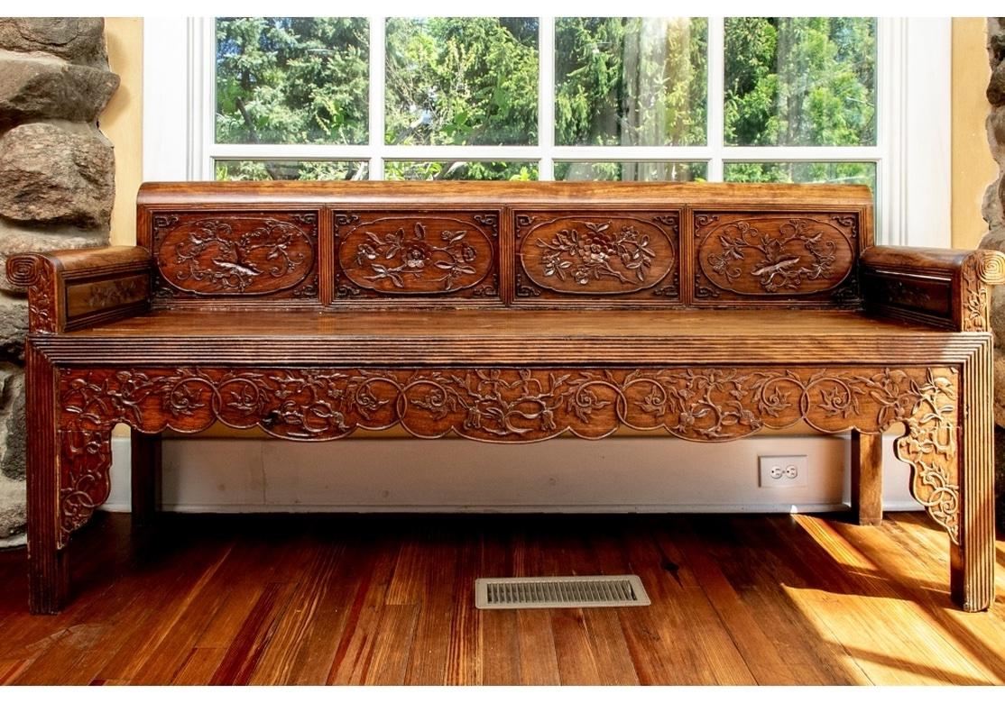 An elaborate and finely carved bench in a pleasing Chestnut tone wood. Scrolled crest rail ends and arm ends. With four carved panels on the back with floral and fruit vines. A reeded skirt rail and with a shaped and carved running band of leafy