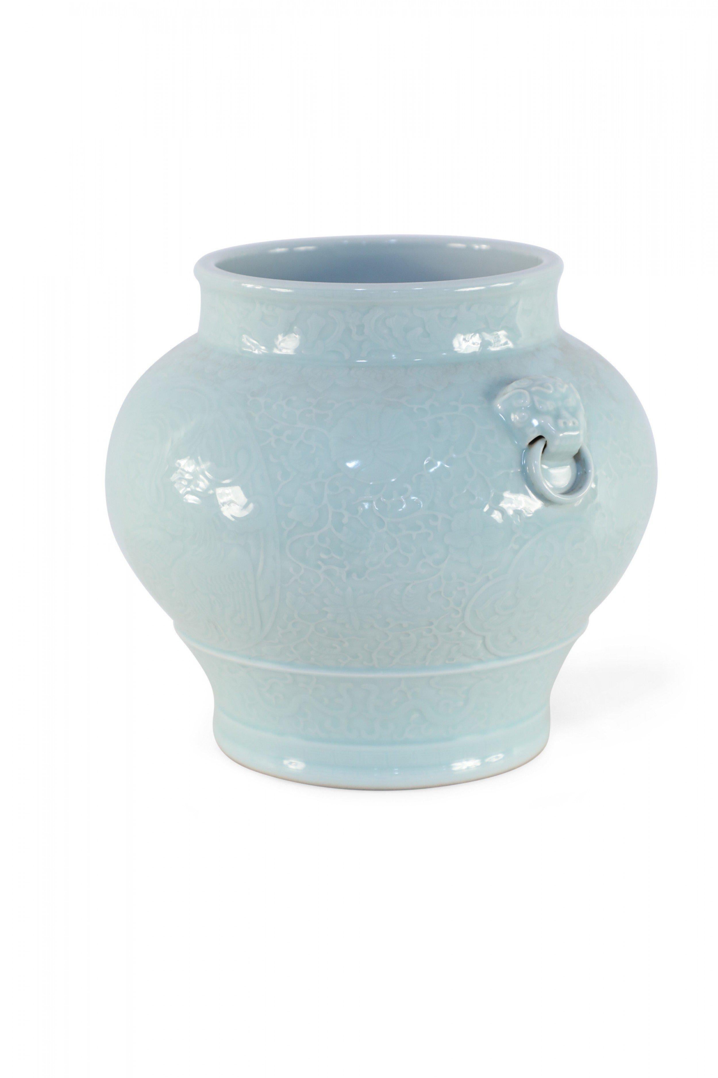 Chinese celadon, porcelain pot decorated with a raised, tonal botanical and dragon design wrapping the entirety of its bulbous form and accented with foo dog door knocker ornamentation along the sides.
