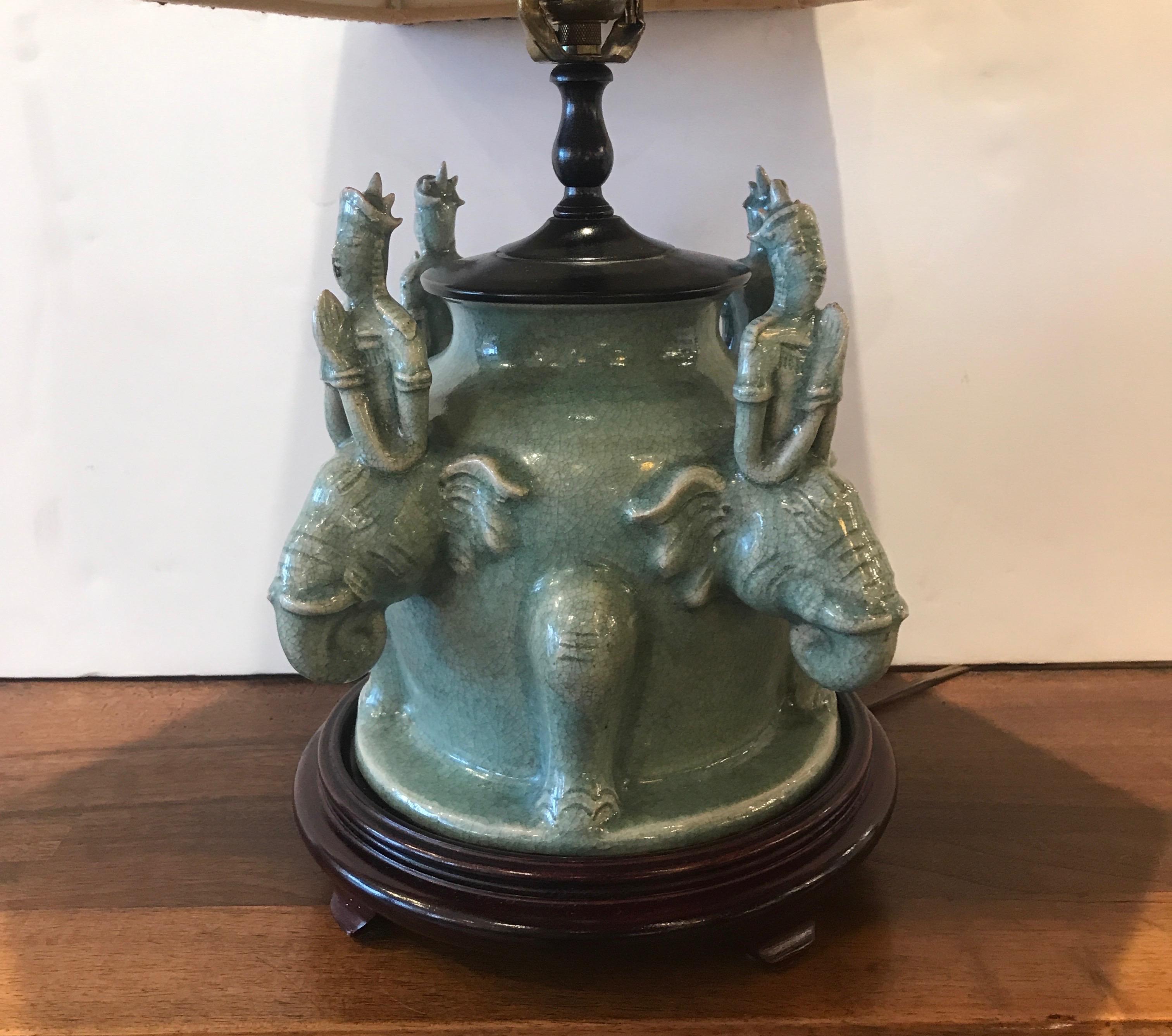 Chinese celedon porcelain lamp with custom shade. The porcelain with four figures of deity and elephant resting on a hardwood base. The shade custom made patterned silk with a jade color stone finial. Very chic decorator style. The base is 9 inches