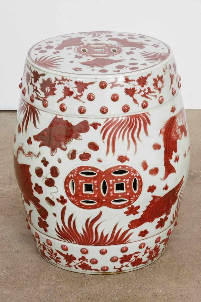 Stunning pair of Chinese ceramic garden stools or drink tables. Featuring a whimsical aquatic life motif with fish and sea grasses. Finished in an oxblood red or sang de boeuf style color over a white ground with pierced sides. The top is decorated
