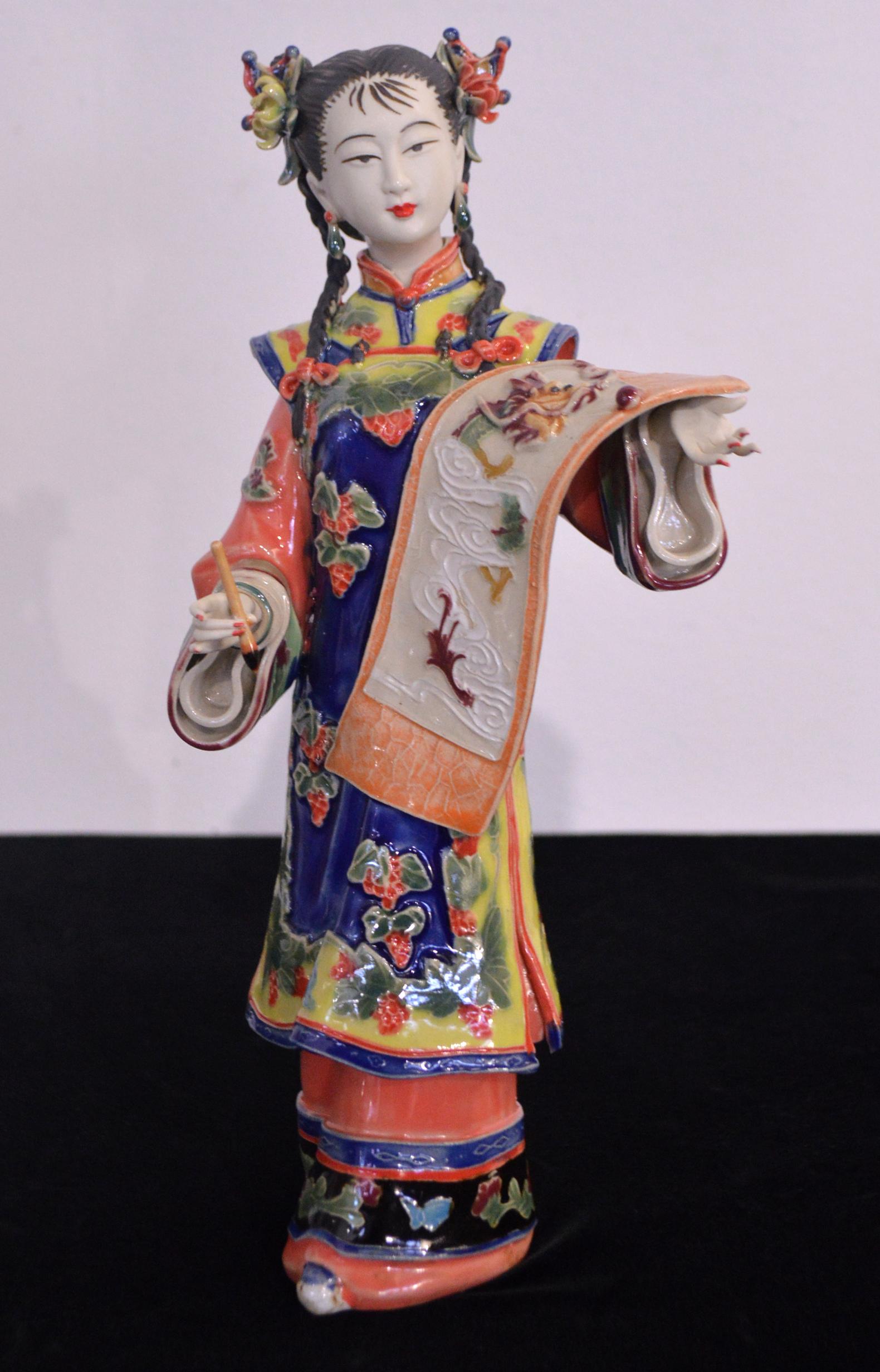This 21st century Chinese ceramic craft production represents a graceful young woman, probably a court lady, painting a dragon. The typical roll is resting on her arms, while the right hand, embellished with a movable bracelet, holds the brush.