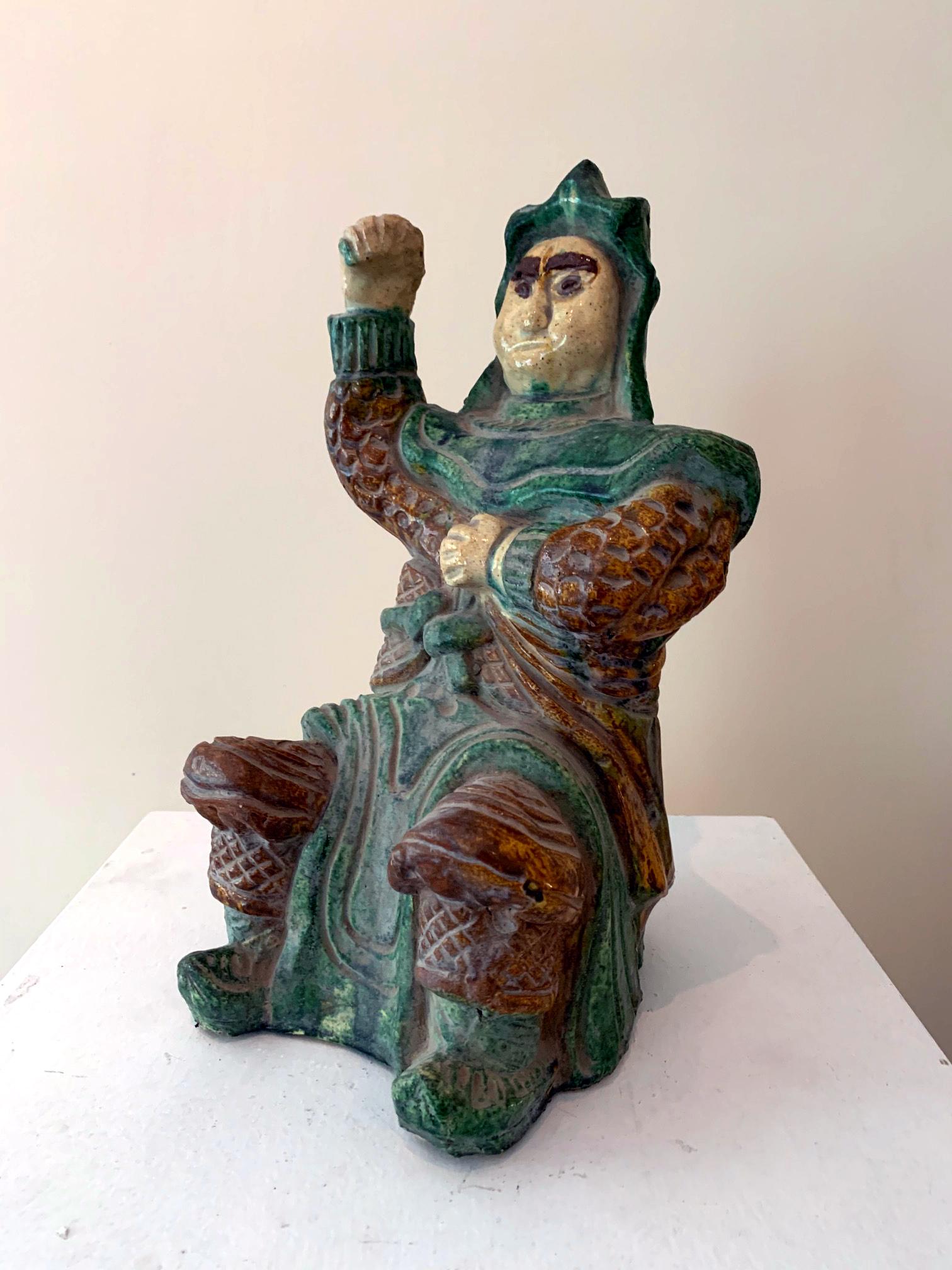 A stoneware figure depicting a seated armored warrior with a striking pose circa 15th-17th century. He is likely one of the four heavenly kings, the protective guardians widely worshiped in China. This figure was heavily molded by hand and the