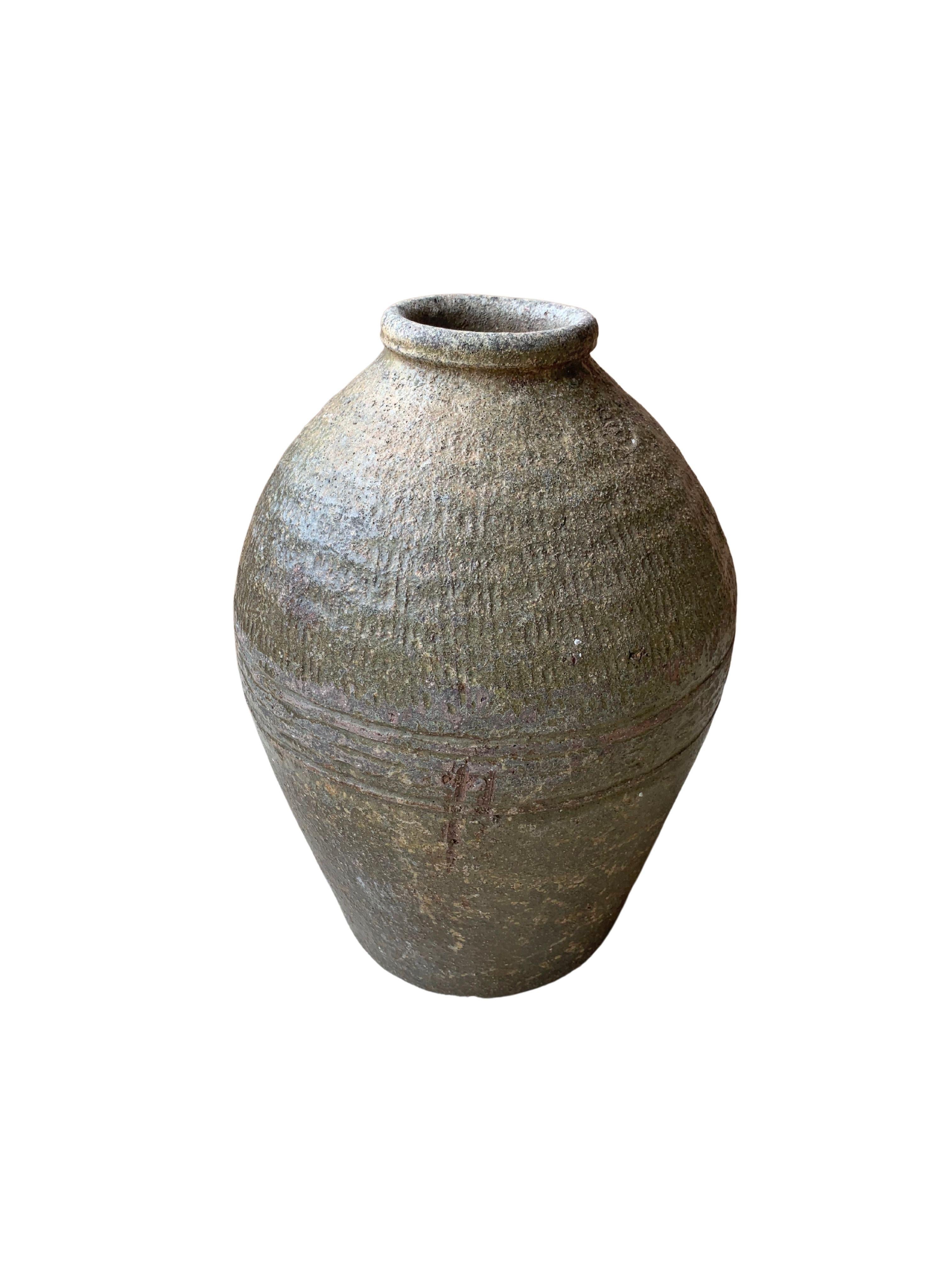 This glazed Chinese ceramic jar was once used for pickling foods. It features a jade green finish and outer surface that features a ribbed texture. A great example of Chinese pottery, with its imperfections and ageing over the years contributing to