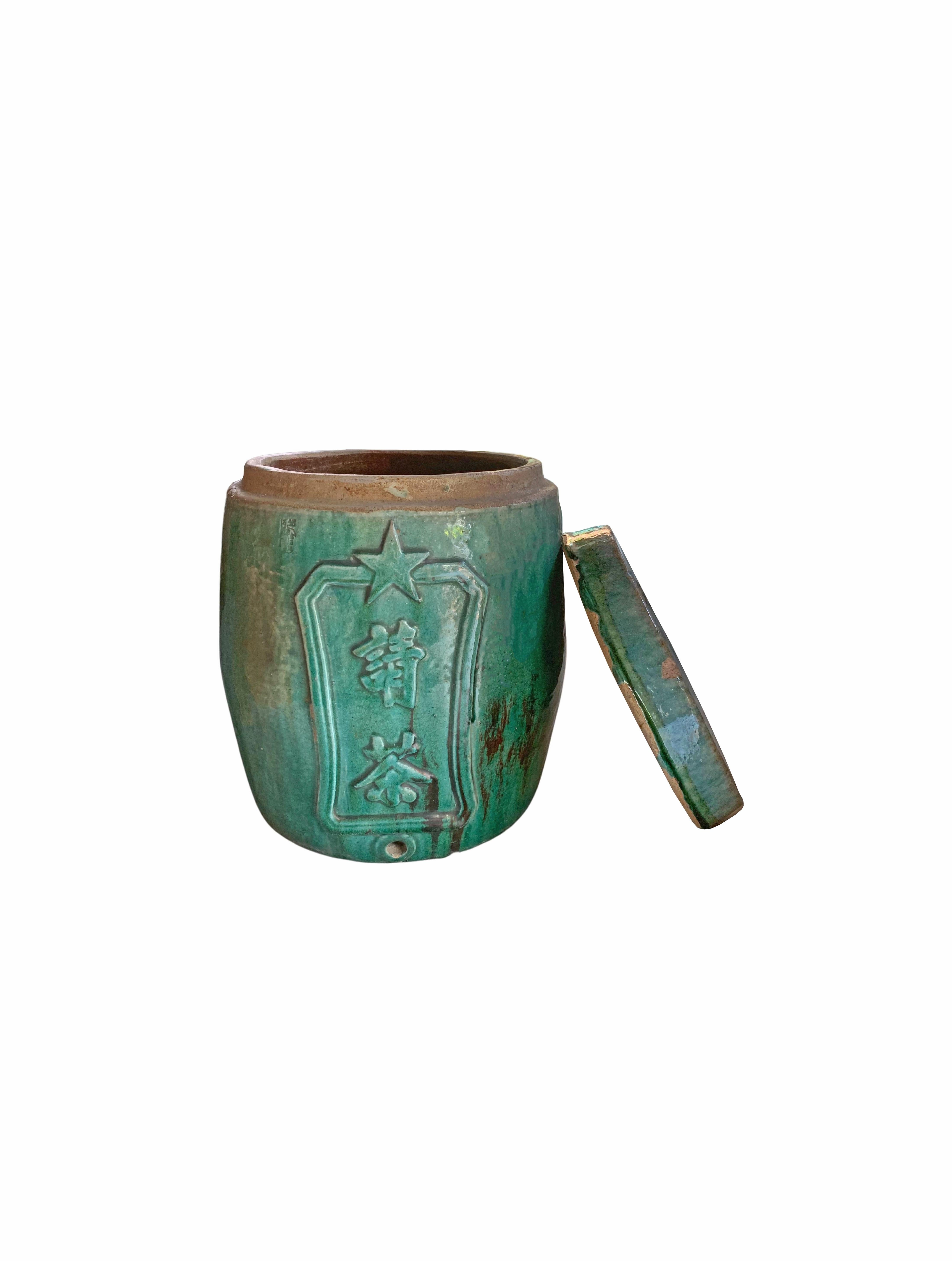 This lidded container of earthenware features a green glaze, known as 'Shiwan Ware' from China's Shiwanzhen district near Guangdong. It was originally used as a tea dispenser hence the small hole on its lower front side. The engraved characters on