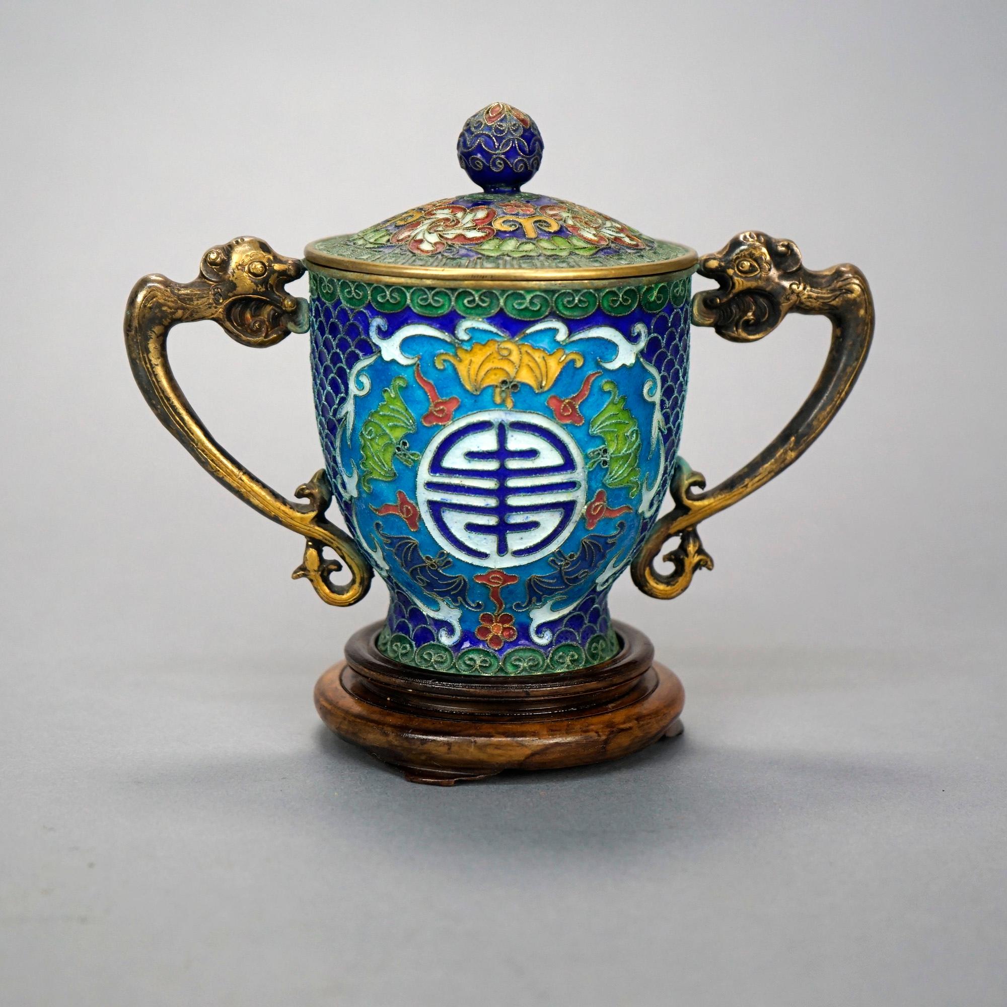 A Chinese covered urn offers Champleve construction with cast double handles in dolphin form, lidded vessel having enameled Good Luck symbol reserve, foliate rams horns and scroll elements, raised on footed base, 20th century

Measures- 5.75'' H x