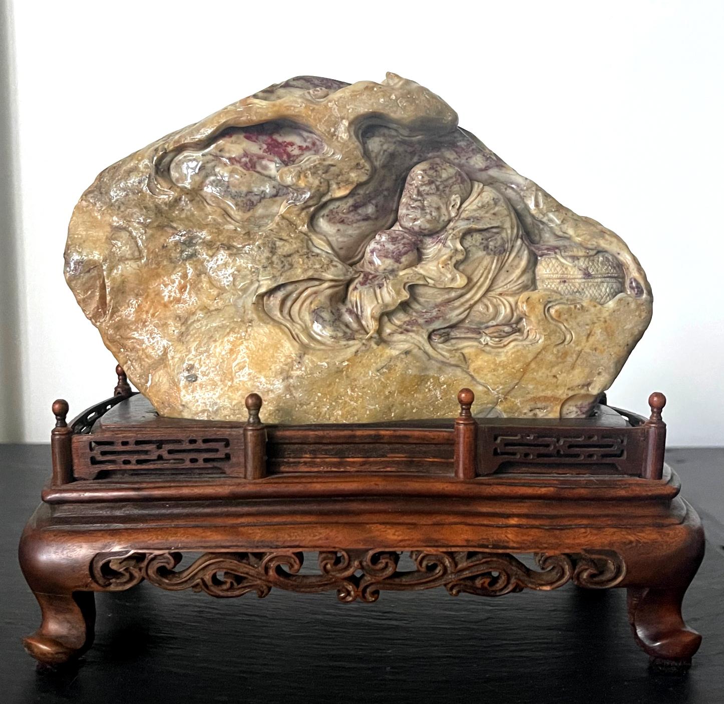 A small chicken blood stone carving from China circa early 20th century, possibly early (late Qing to early Republic period). It depicts an aged Bodhidharma meditating in a cave. The stone was identified as chicken blood stone, a rock of