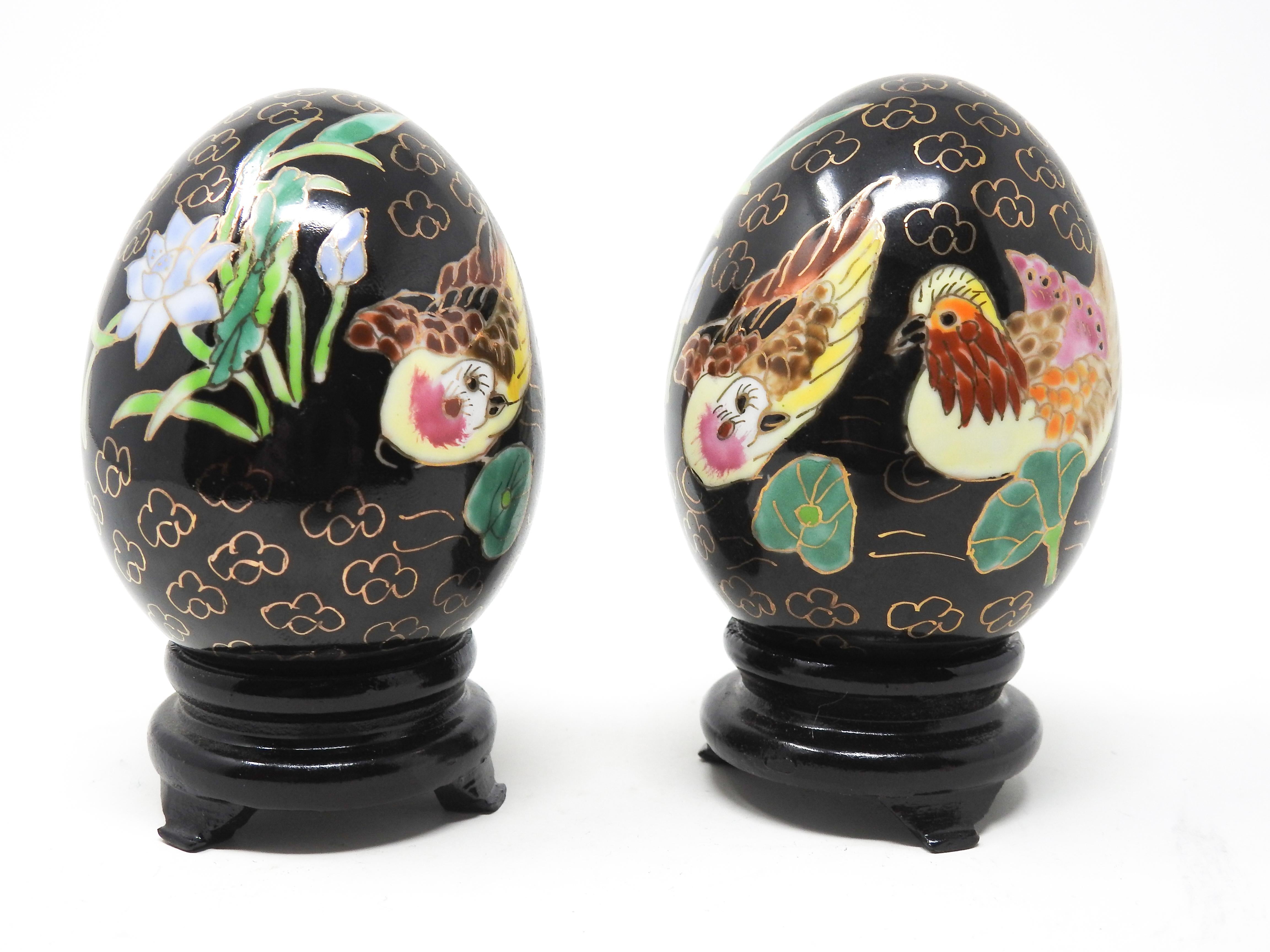 Offering this pair of Chinese chinoiserie enamelware eggs. The background is in a dark black, and has gold puffs on most of the surface. There are two hens depicted in vibrant colors, and to either side of them foliate and floral designs. The eggs
