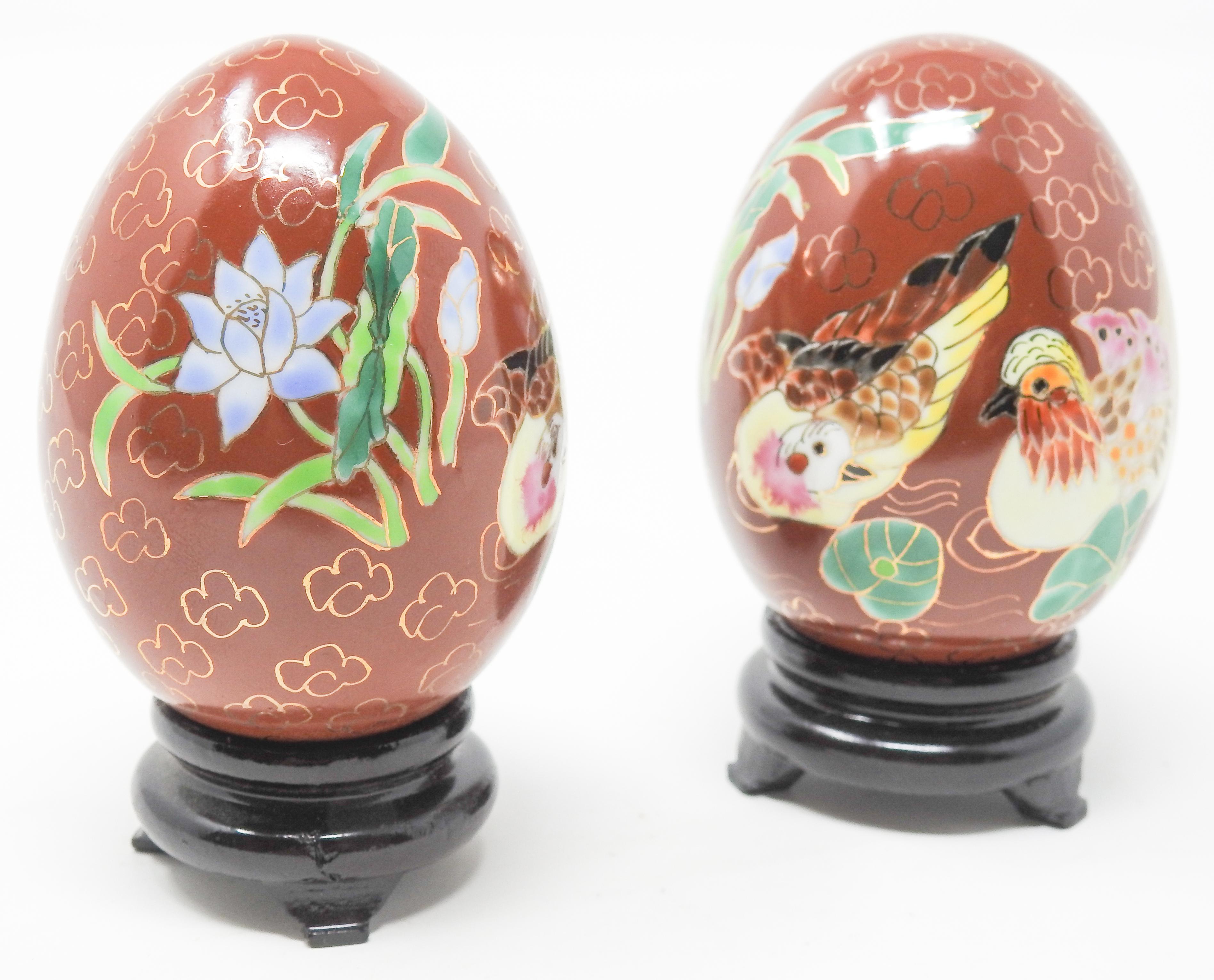 Offering this pair of Chinese chinoiserie enamelware eggs. The background is in a Chinese red, and has gold puffs on most of the surface. There are two hens depicted in vibrant colors, and to either side of them foliate and floral designs. The eggs