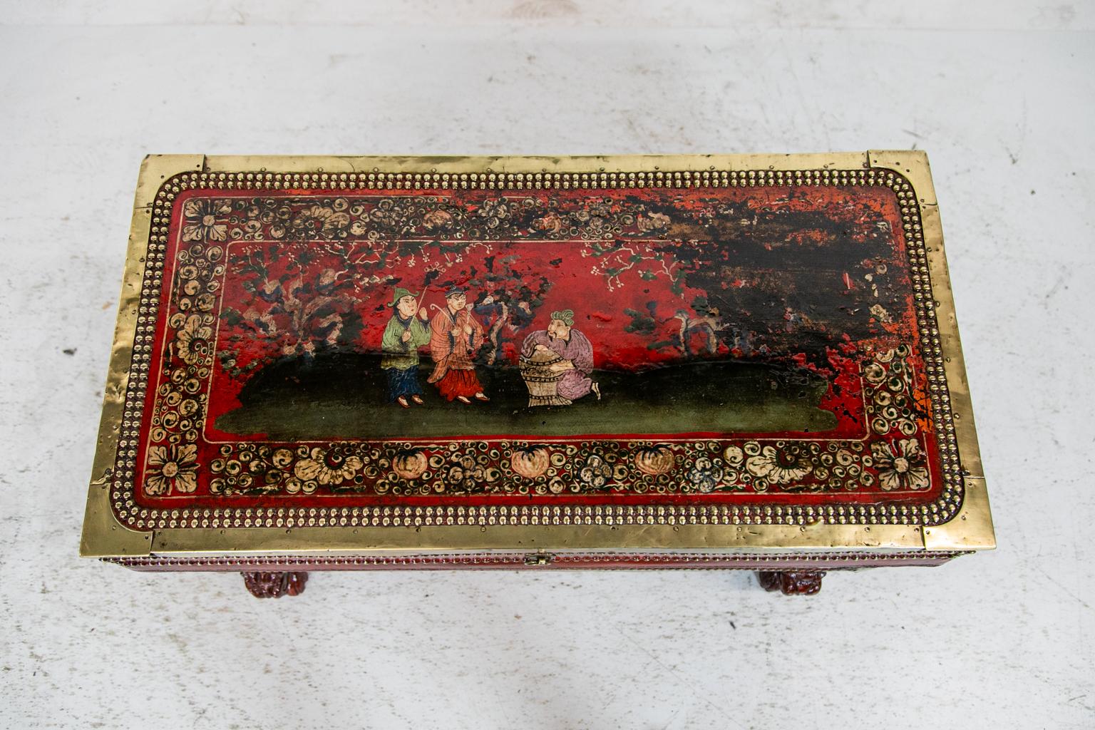 This Chinese chinoiserie trunk is bound with solid brass edging and has chinoiserie and floral painting on a red background. The chinoiserie decoration, painted on leather, is on the top, front, and sides. There Is noticeable wear to some of the