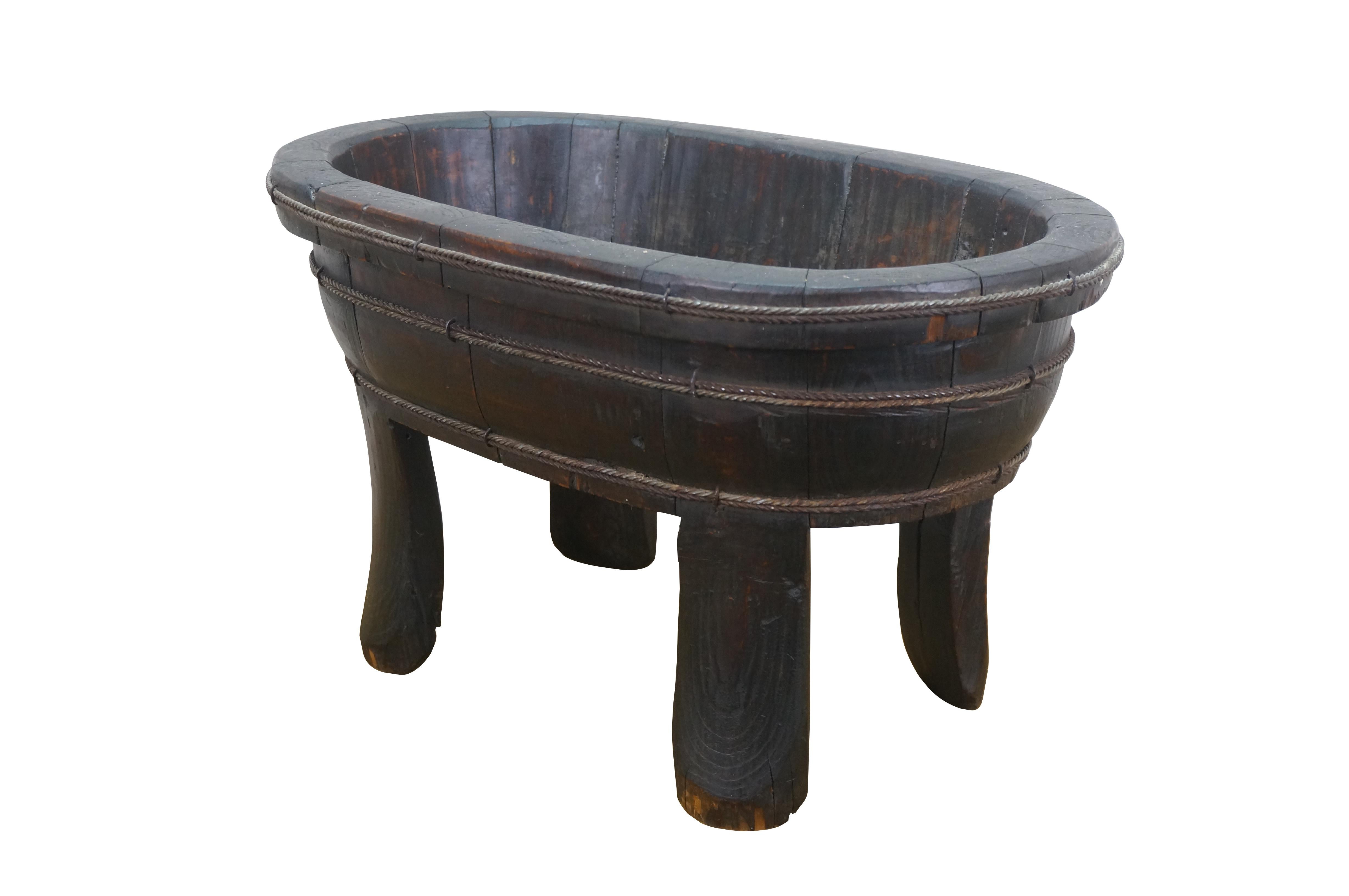 Chinese Chinoiserie wooden laundry tub/wash basin/planter - oval shape with slatted barrel-like sides, supported on four gently curved legs/feet, and banded with three rows of rope twist iron cords. The interior base is impressed with a trio of