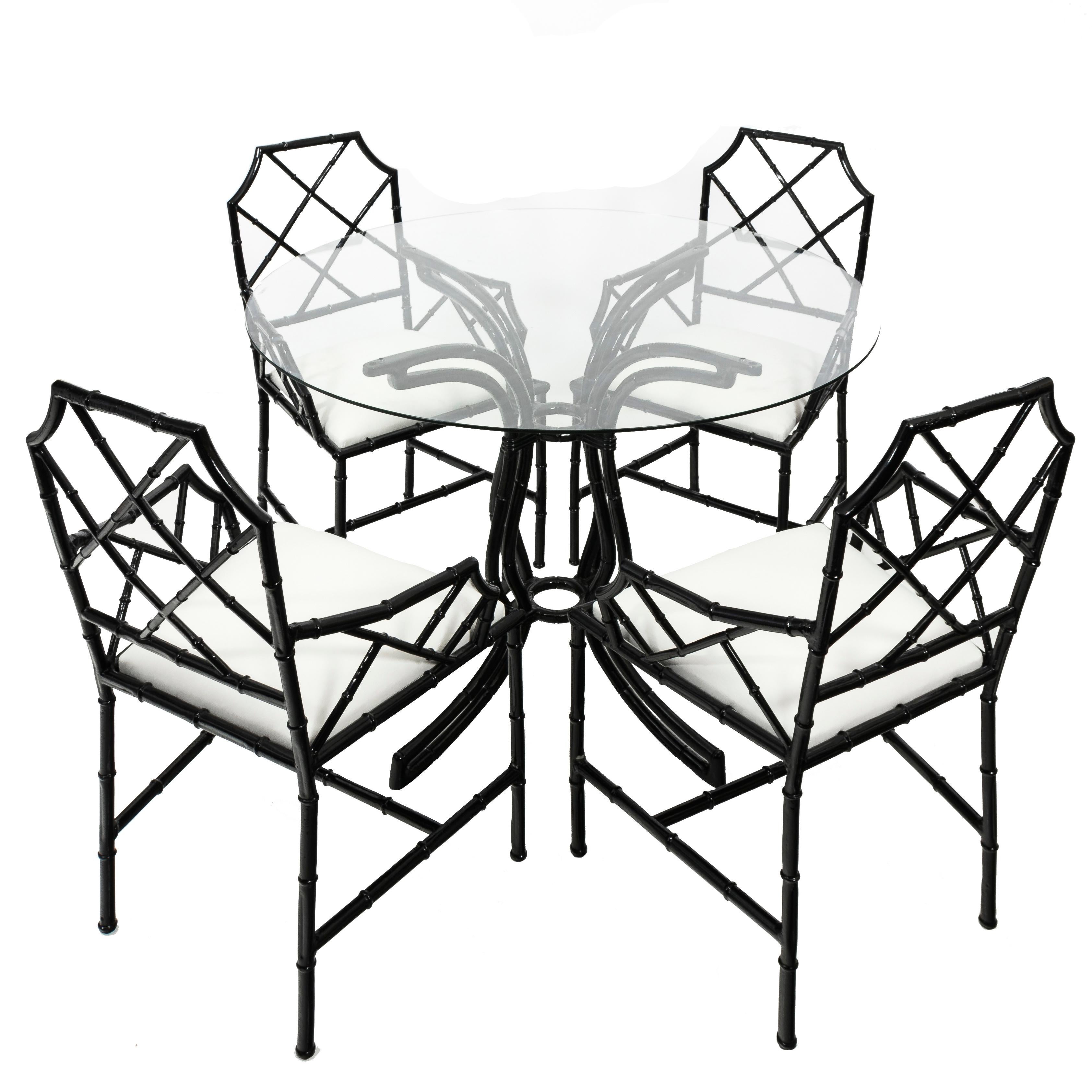 Set of four black Chinese Chippendale-style metal bamboo chairs. Newly powder coated in black gloss finish. Newly upholstered in white indoor/outdoor linen fabric. Table has a new clear glass round top. Suitable for indoor or outdoor use. Table is