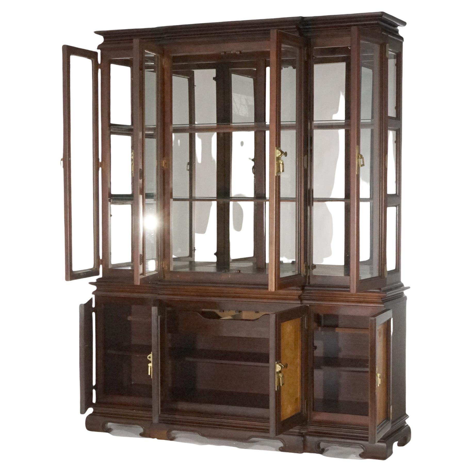 A Chinese Chippendale style breakfront cabinet offers mahogany construction with upper having glass doors opening to shelved, mirrored and lighted interior; lower with four doors with burl panels and opening to shelved interiors, 20th