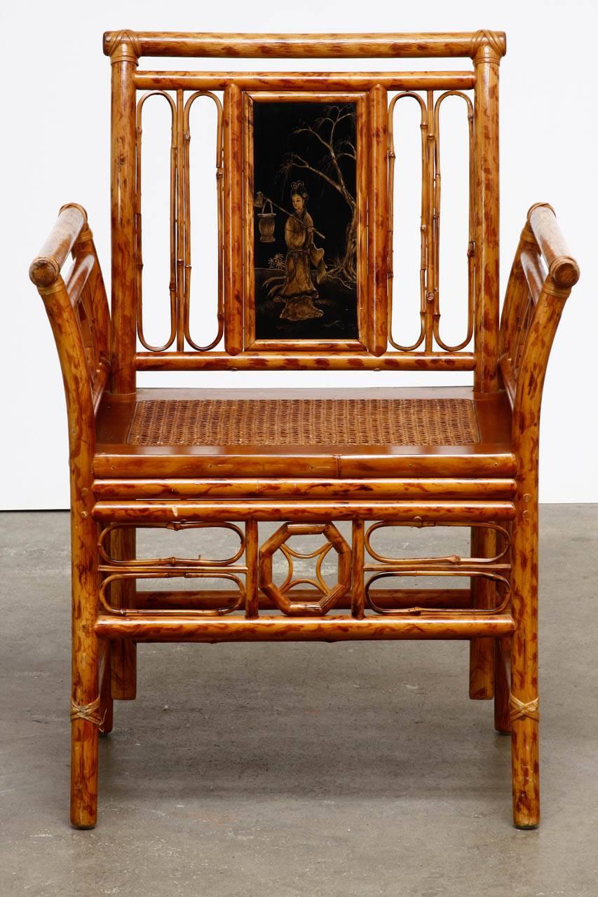 Distinctive bamboo and cane armchair made in the Chinese Chippendale manner featuring decorative open fretwork arms, back, and apron. The backsplat has a Japanned and lacquered panel with a beauty by a tree. The caned seat is supported by round