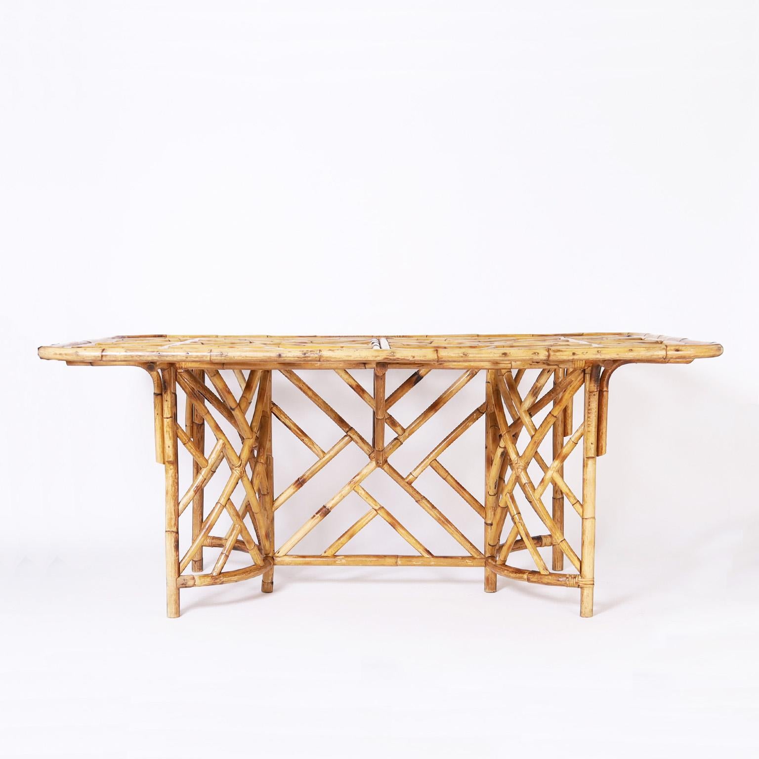 Impressive mid-century table crafted in bamboo and bent bamboo with Chinese Chippendale elements on the top, concave supports and center joining panel. Complete with a glass top. 