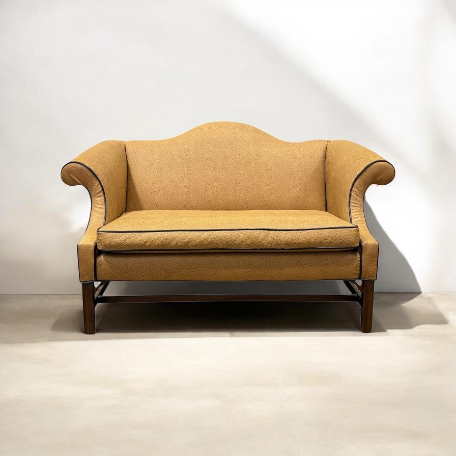 This is a Chinese Chippendale style camelback settee in a gold ostrich leather. The welting is black. The frame is a carved mahogany. It is unmarked and in very good vintage condition. It was manufactured in the United States in the later part of