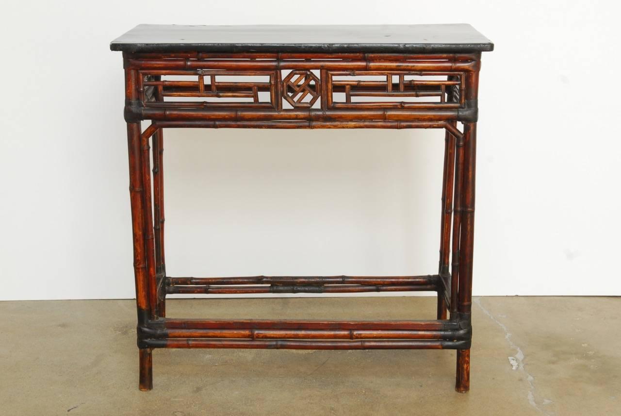 Elegant lacquered wood and bamboo lattice fretwork console table made in the Chinese Chippendale style. Features a black lacquered wood top panel with a decorative lattice fretwork geometric design on three sides. Supported by bamboo legs conjoined