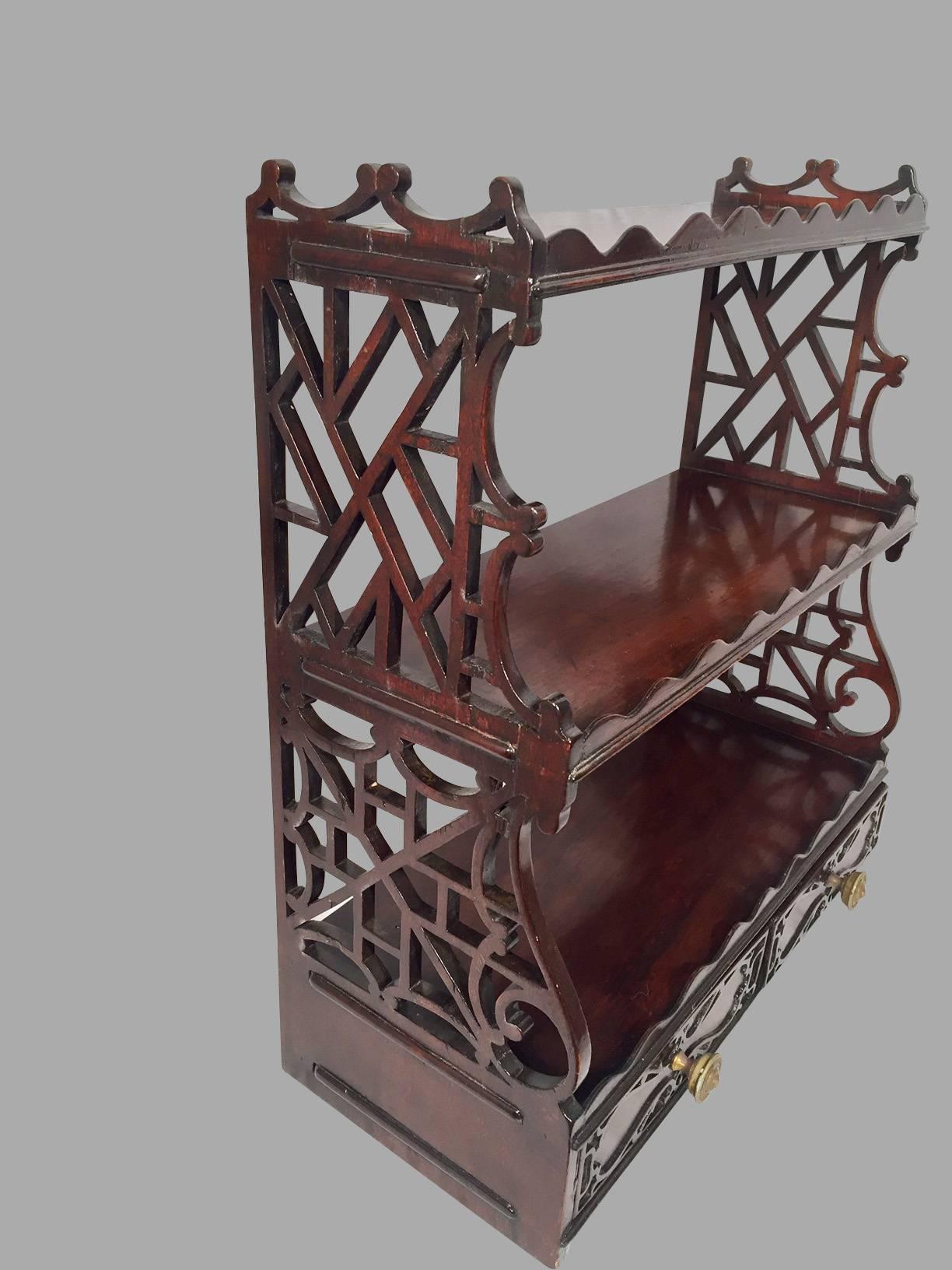 A Chinese Chippendale style hanging shelf with elaborate open lattice sides, each shelf with a scalloped front edge, the base with two short drawers decorated with applied fretwork.

      