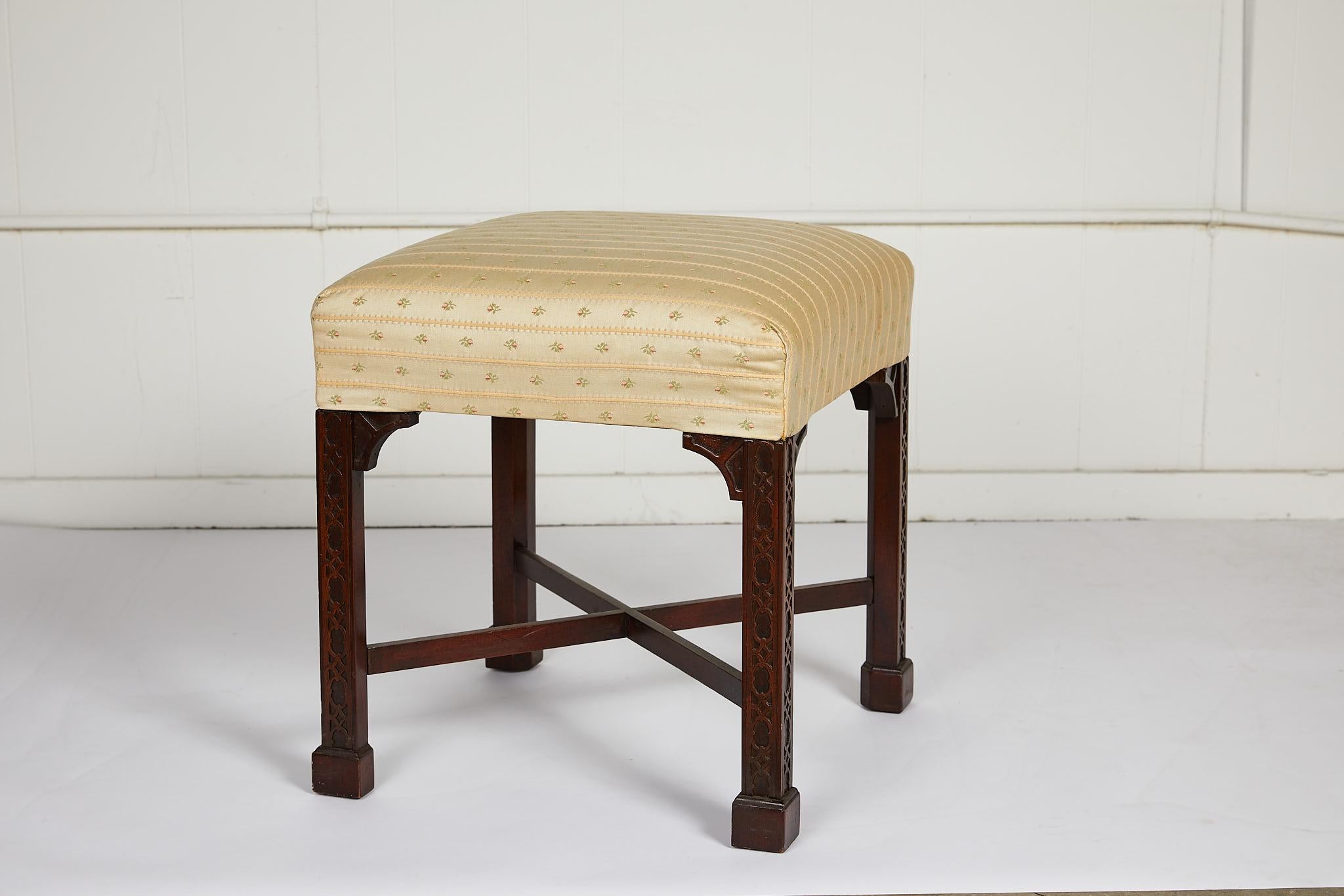 Charming 19th century English carved mahogany stool in the Chinese Chippendale style with four square fretwork carved legs and block feet joined by an X stretcher. The stool is upholstered in a delicate miniature floral and stripe, and the fabric is