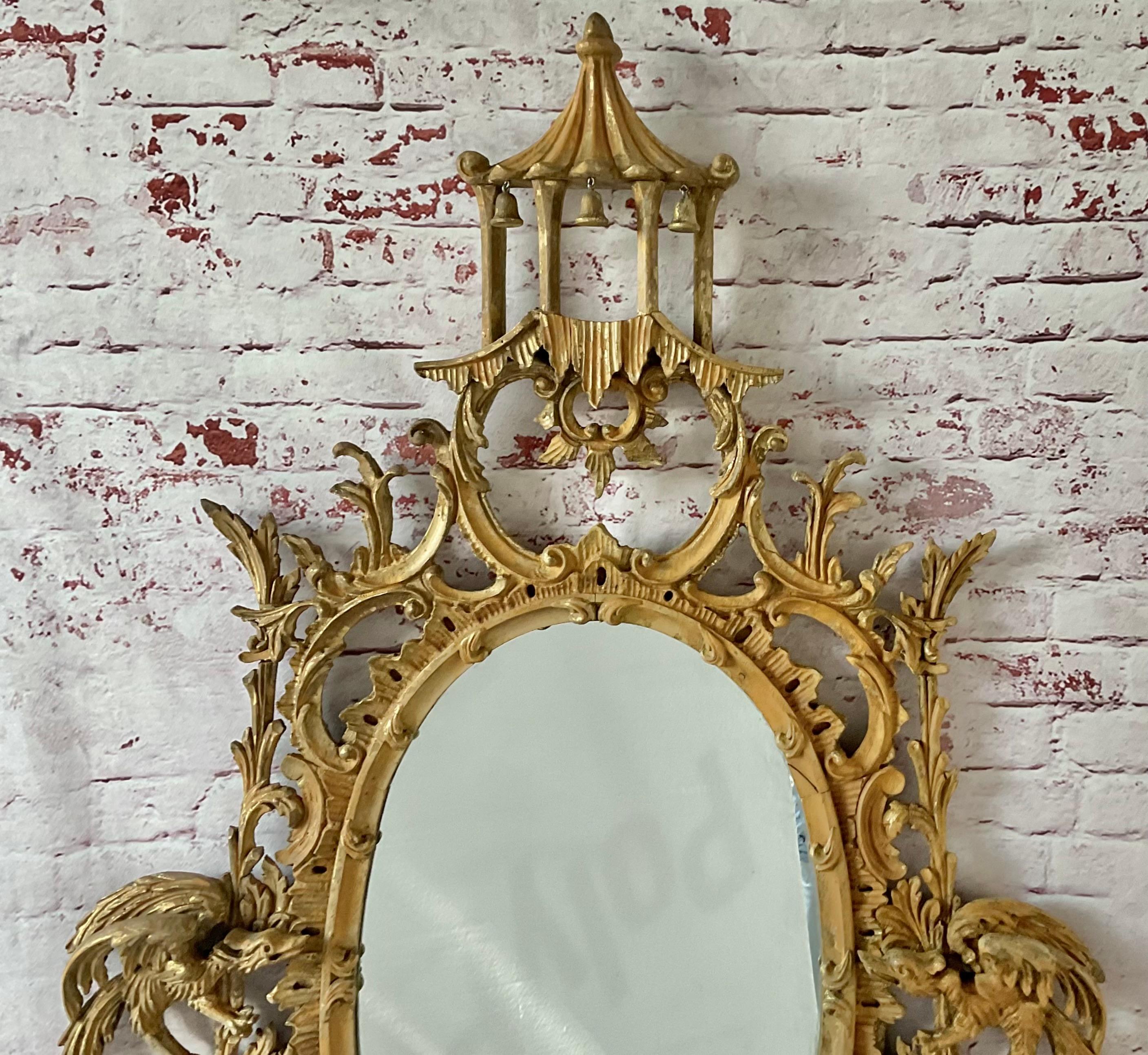 20th Century Chinese Chippendale Style Oval Mirror. Mirror features an oval mirror plate framed by an intricately carved giltwood surround, and is crowned with a pagoda-style carved crest, and further carved with phoenix birds and scrolling foliage