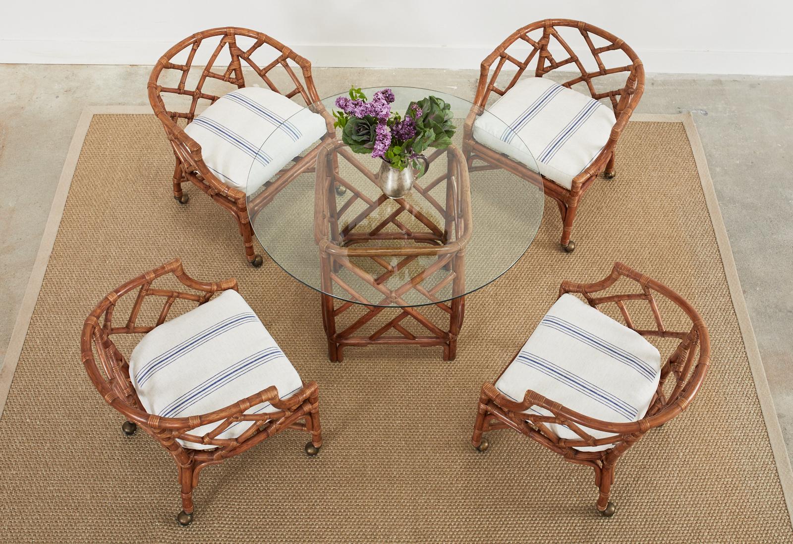 Gorgeous suite of Chinese Chippendale style dining chairs and table crafted from rattan. The suite consists of four barrel back formed rattan dining armchairs and a matching dining table. The chairs and table have a lovely open fretwork design made