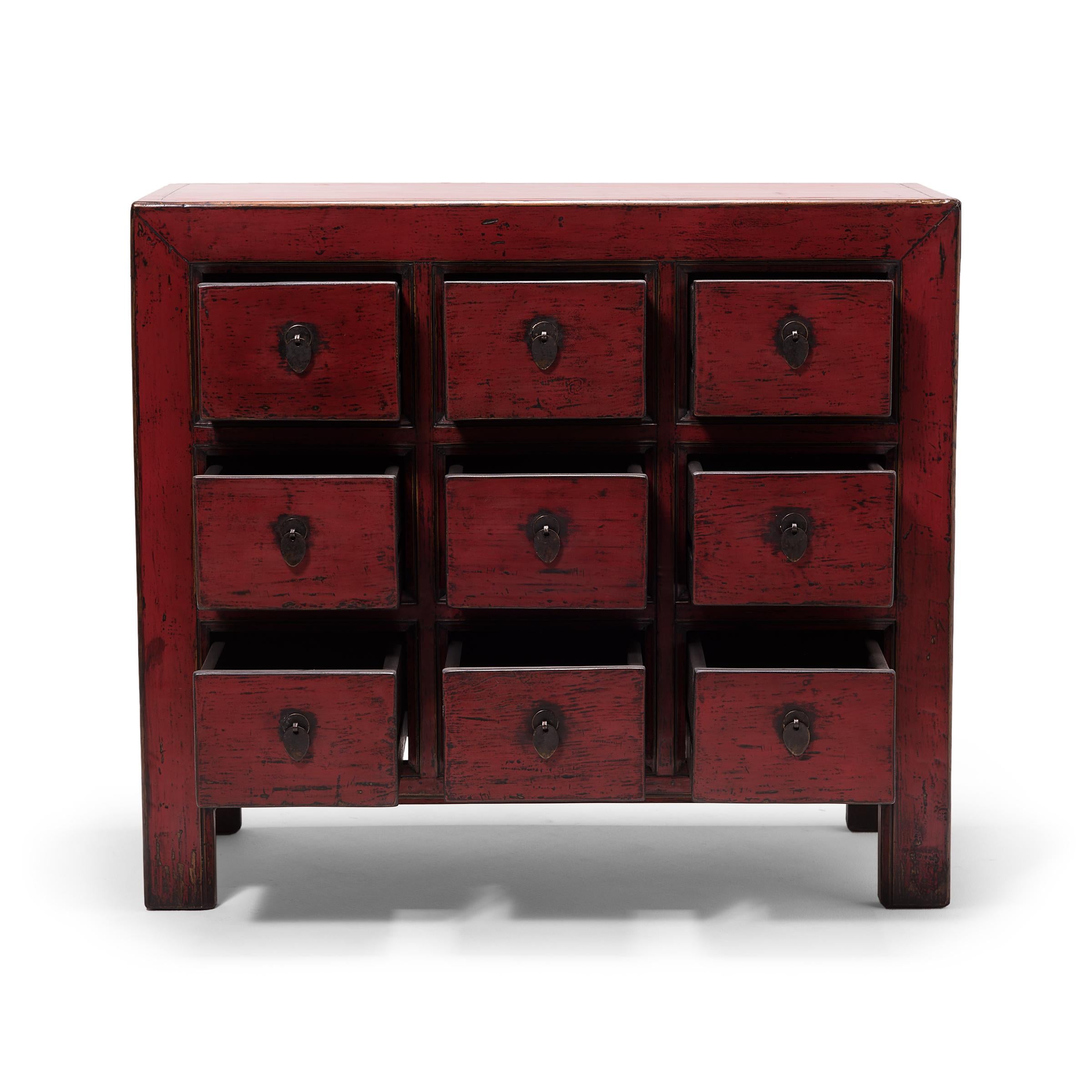 This contemporary apothecary chest is modeled after those used in Qing-dynasty pharmacies to organize and store herbal medicines. A statement piece cloaked in a crimson red lacquer, the cabinet has nine drawers, each punctuated by a teardrop brass