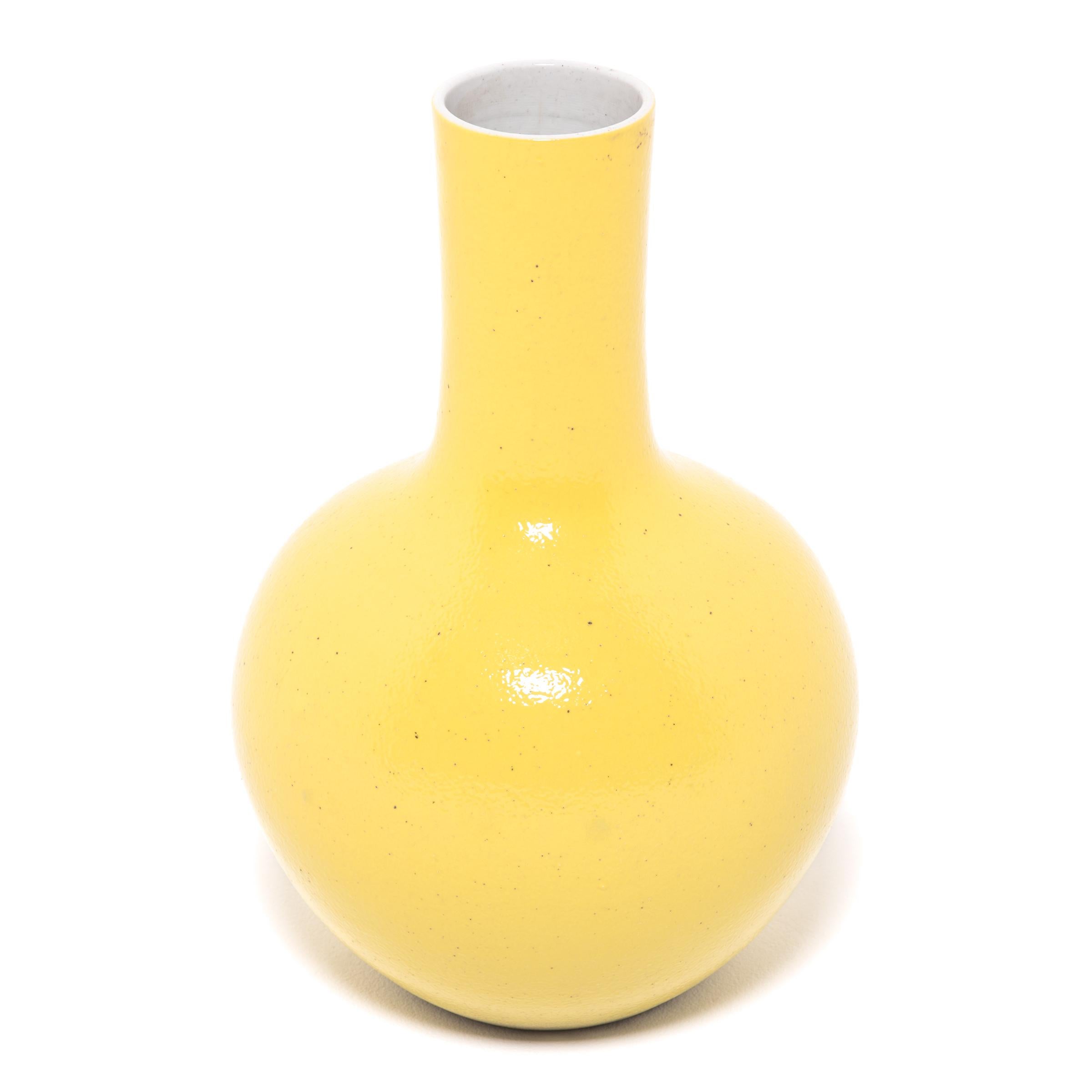 Drawing on a long Chinese tradition of ceramics, this striking long-necked vase is cloaked in an all-over citron-yellow glaze. With a rounded, globular body and cylindrical neck, the large vase reinterprets the traditional gooseneck shape known as a