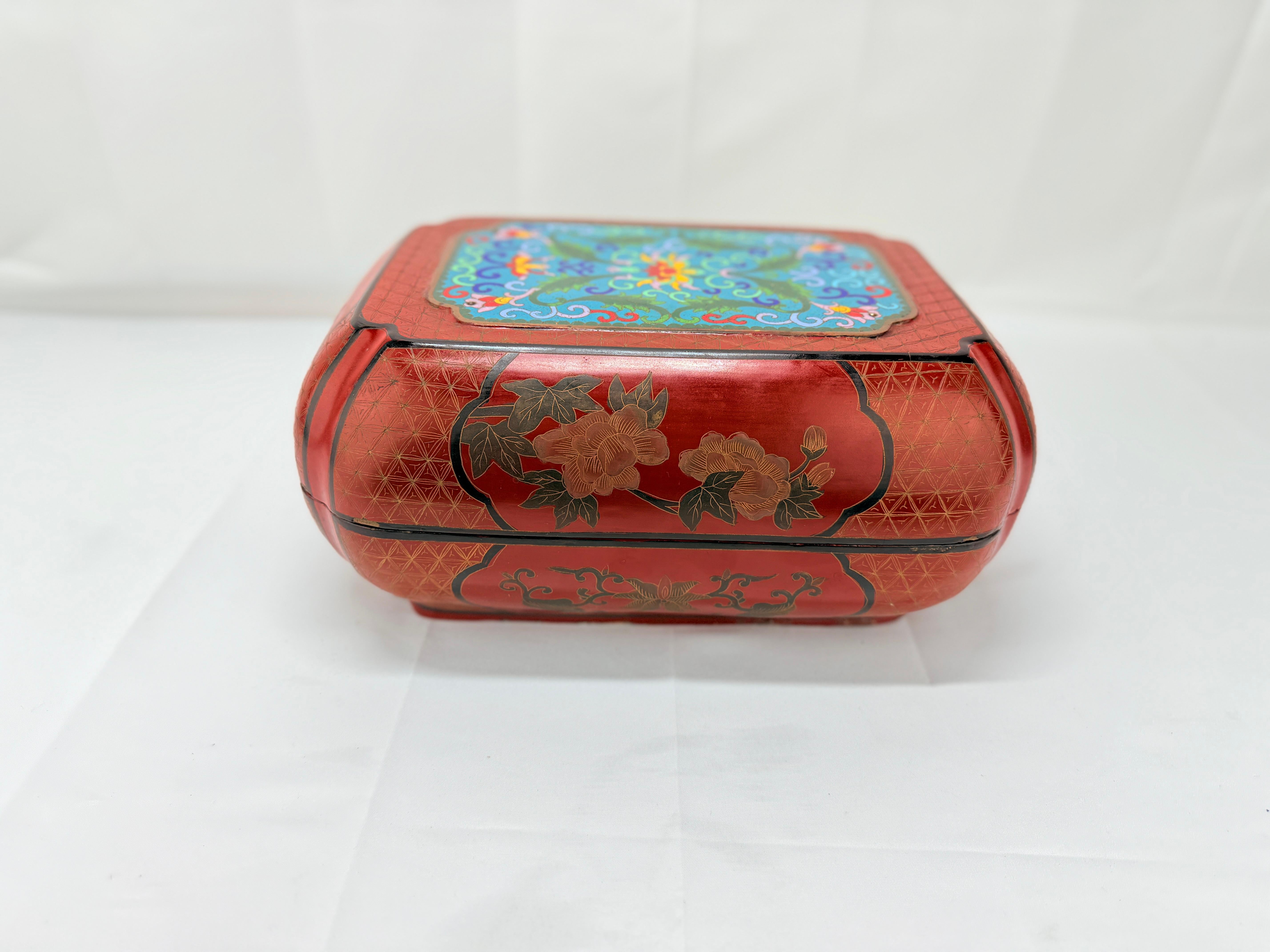 Se trata de una preciosa caja lacada con montura de esmalte cloisonné, que presenta un intrincado diseño que combina la artesanía tradicional con un vibrante arte. La tapa presenta un panel central ricamente coloreado, adornado con motivos florales