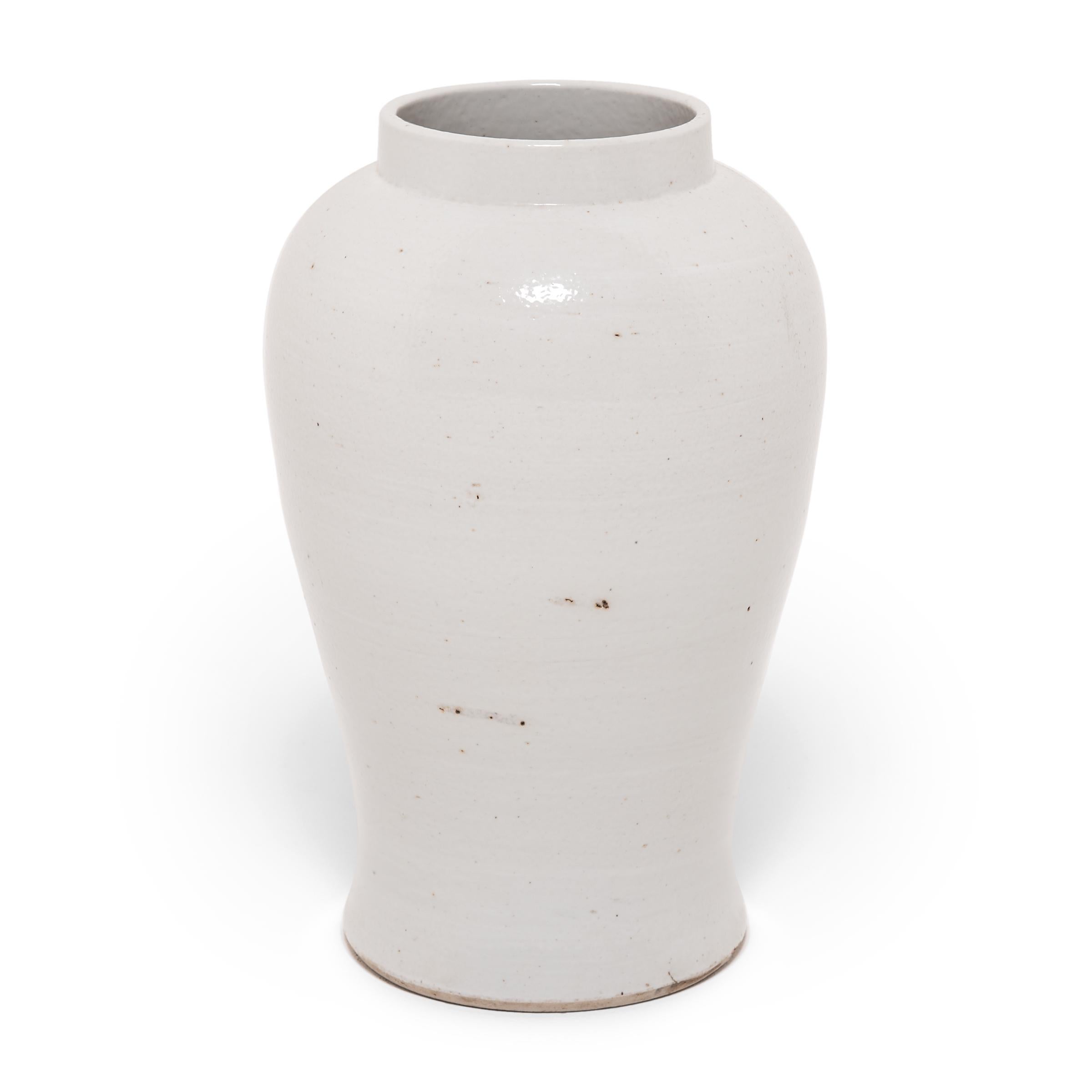 Shaped with high shoulders and a slightly flared base, this porcelain vase is defined by its clean lines and gentle curves. Traditionally elaborately decorated, this modern take is on the baluster jar is cloaked in a simple, milky white glaze to