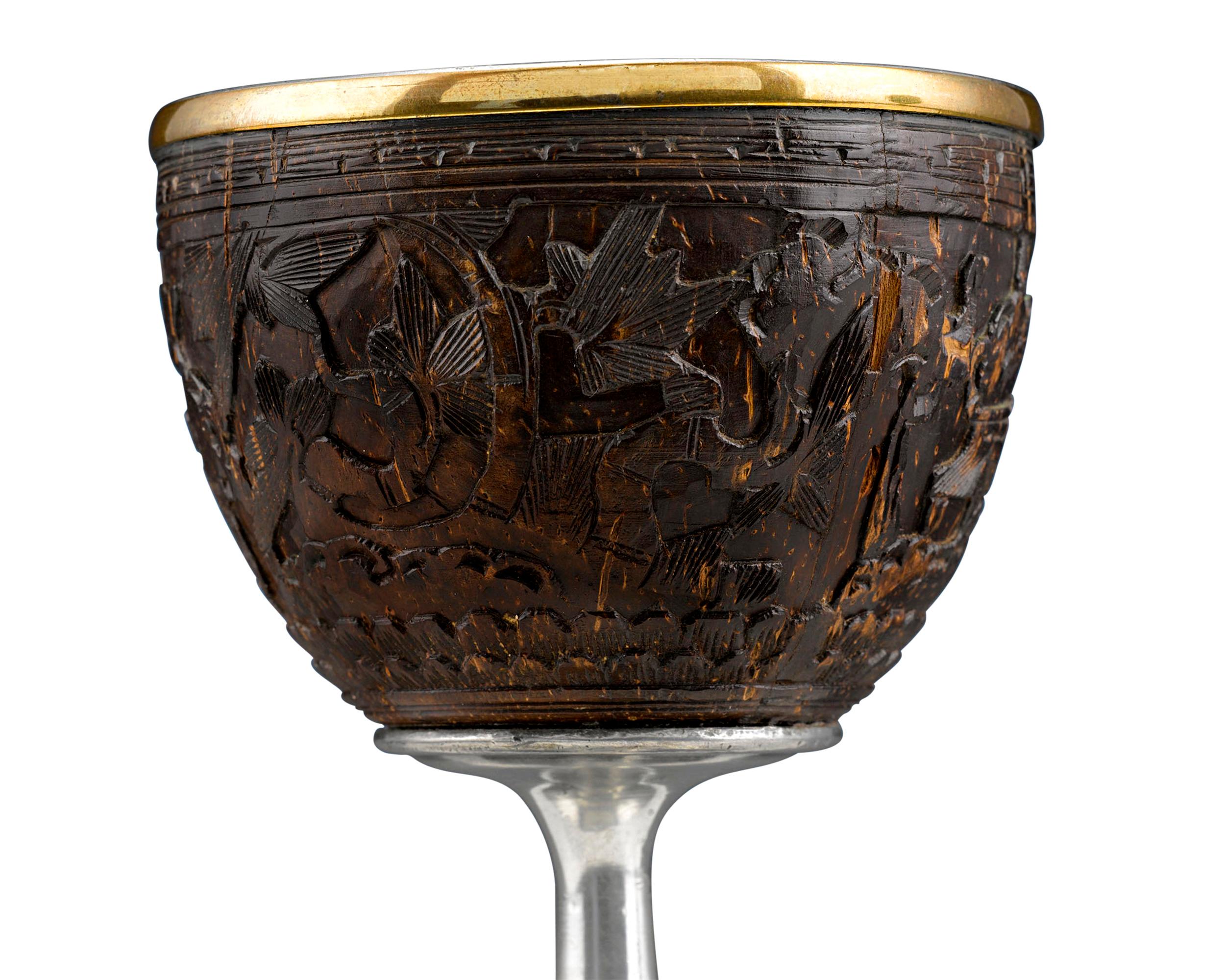 Carved from the shell of a coconut, this enchanting Chinese cup exhibits exceptional artistry. An elegant floral design encircles the entire cup, while the interior is fully lined with silver. In addition to the poison detecting powers attributed to