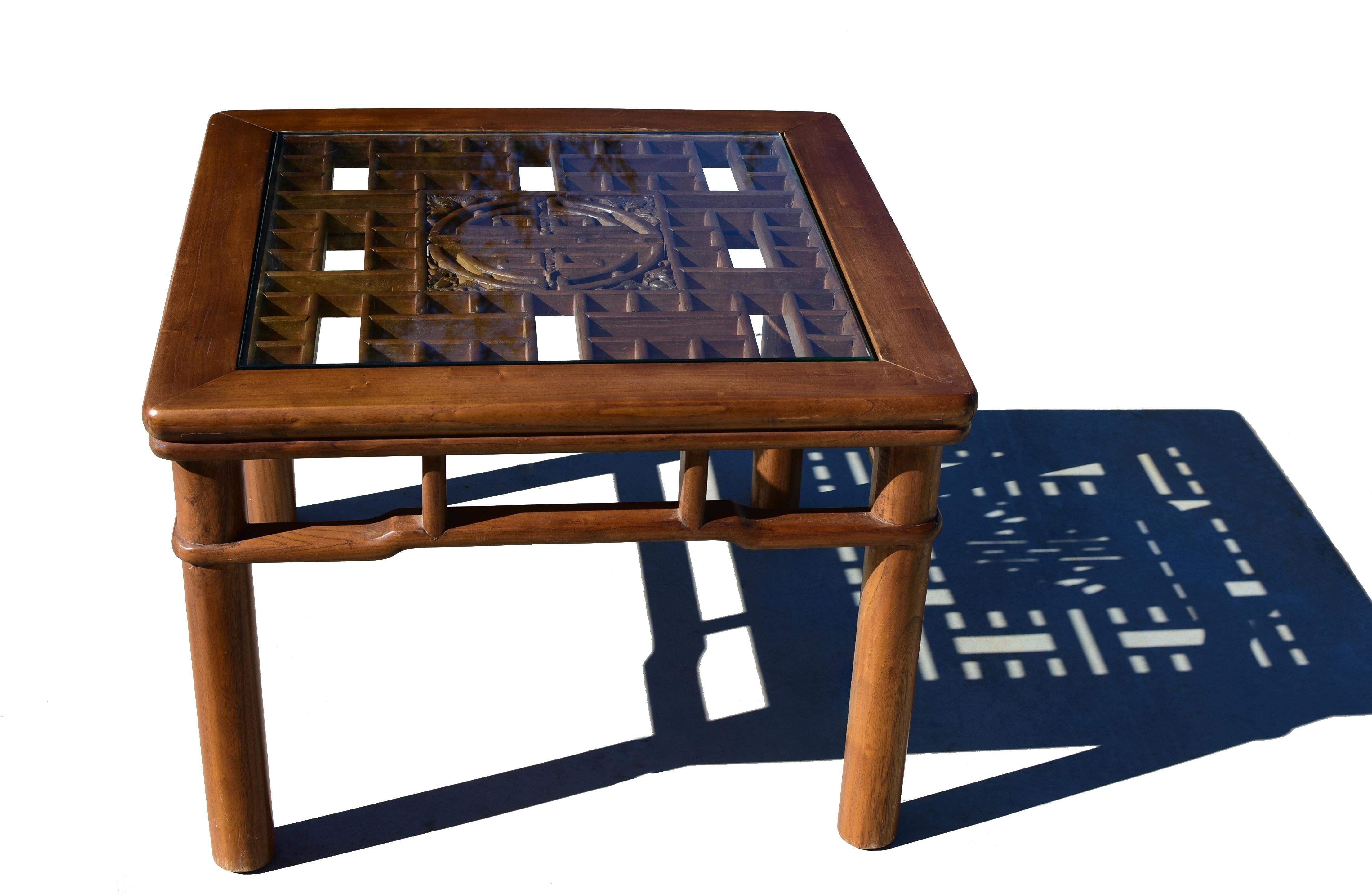 Une belle table carrée en finition naturelle, fabriquée en bois d'orme massif. Le plateau de la table garni d'un écran ancien présente des coins arrondis et des entourages sculptés créant une double illusion. Le plateau de la table se poursuit par