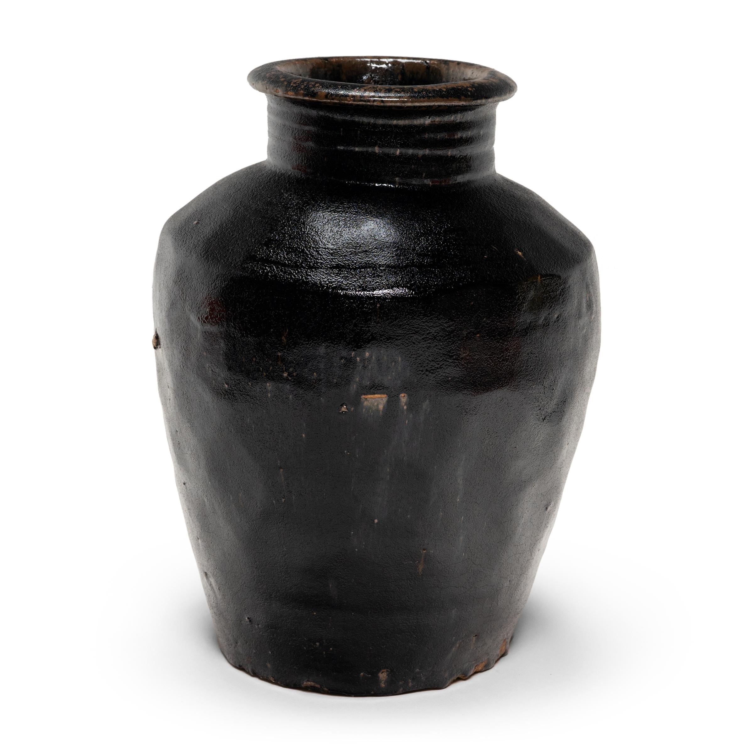 Originariamente utilizzato per la fermentazione del riso o del sorgo in aceto, questo vaso di terracotta dell'inizio del XX secolo è rivestito all'interno e all'esterno da una spessa glassa scura. Lo smalto nero inchiostro si stende e si accumula