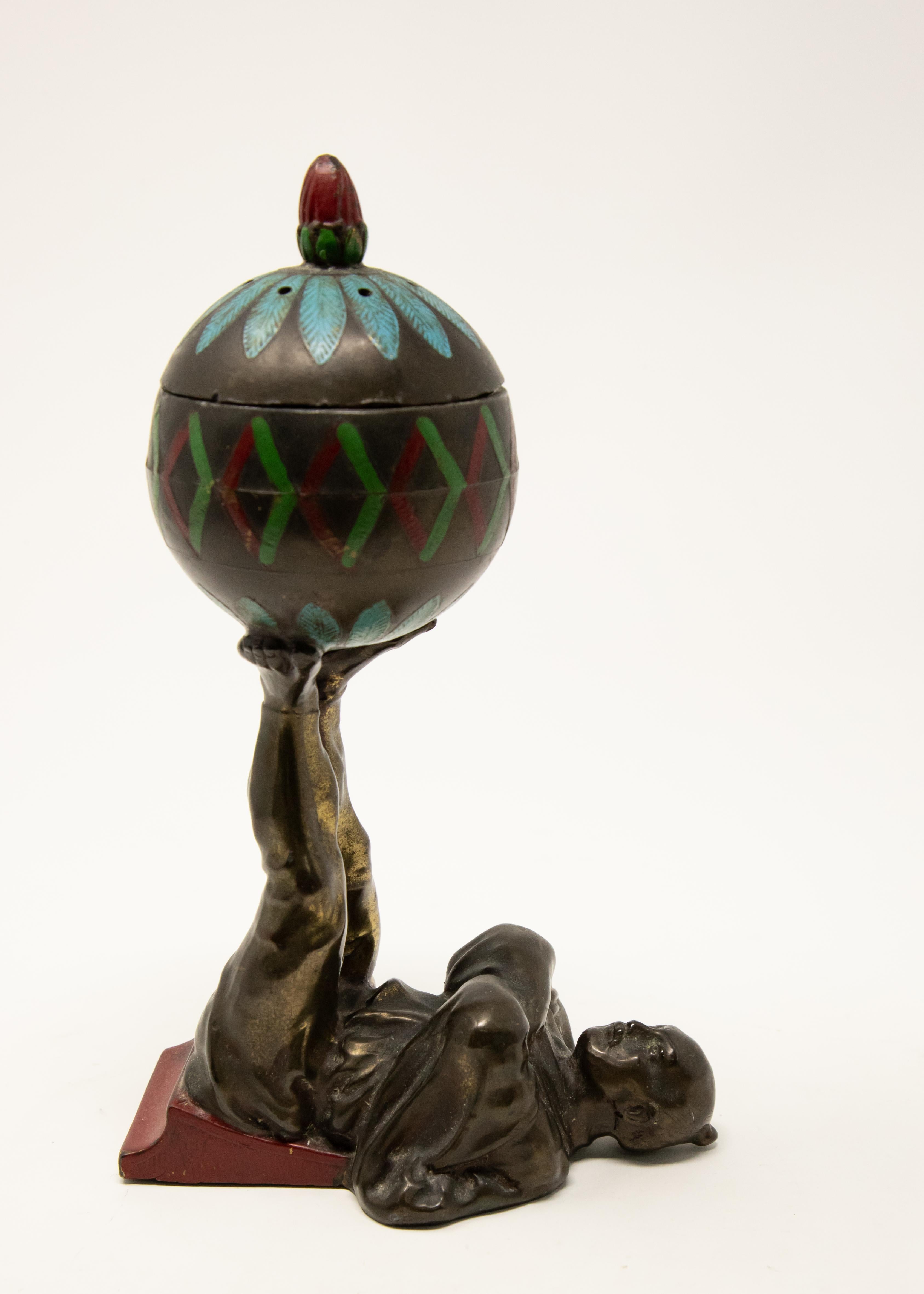 Offering this unusual cold-painted bronze European Chinoiserie censer. The base is a man lying on his back with a wedge under his legs. The legs are together and upward holding a sphere. The sphere is cold-painted with geometric designs. The sphere