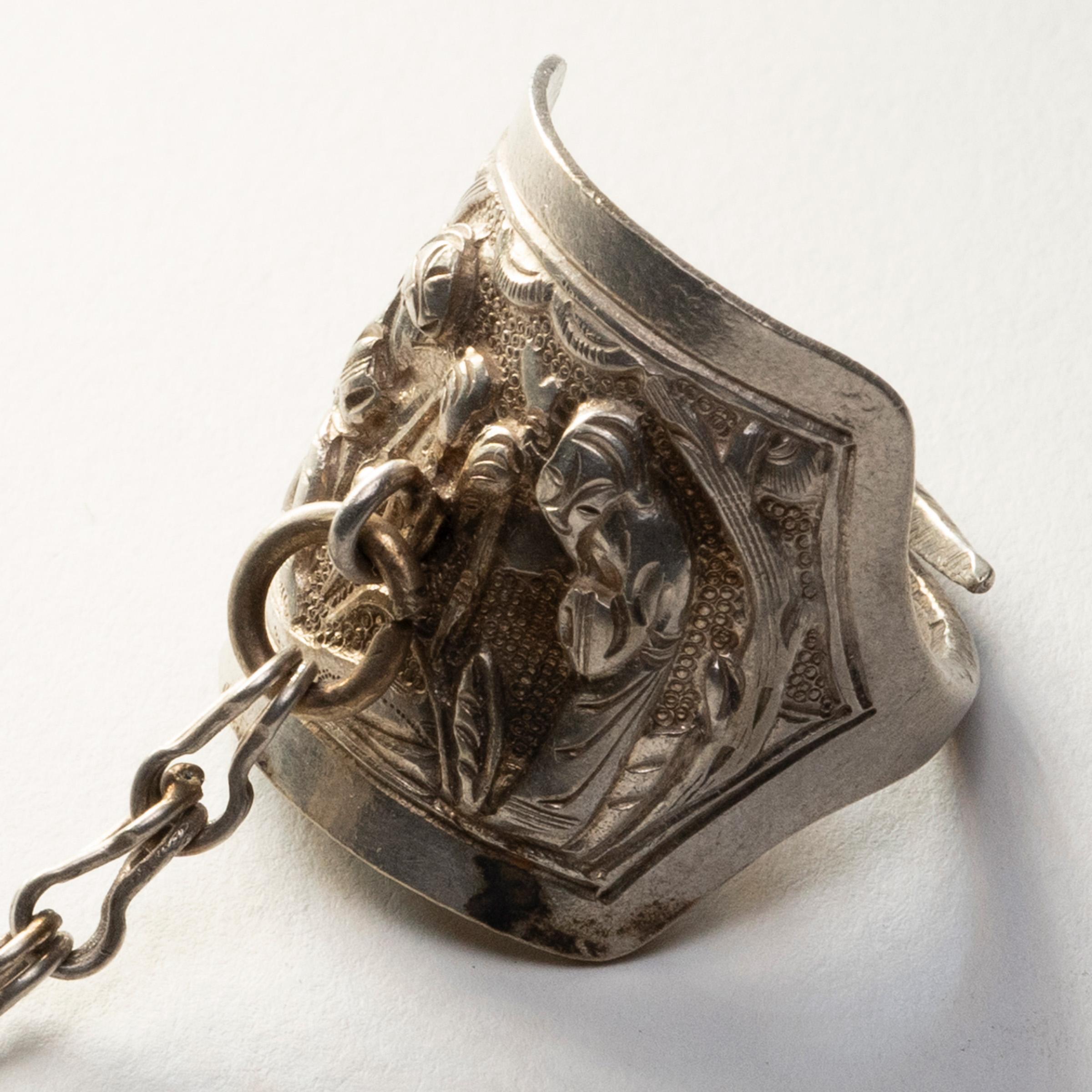 Dated to the late 19th century, this silver charm ring was believed to protect the wearer from bad luck and malevolent spirits. The ring is decorated in relief with a scene of two robed scholars strolling through a garden, surrounded by pine trees