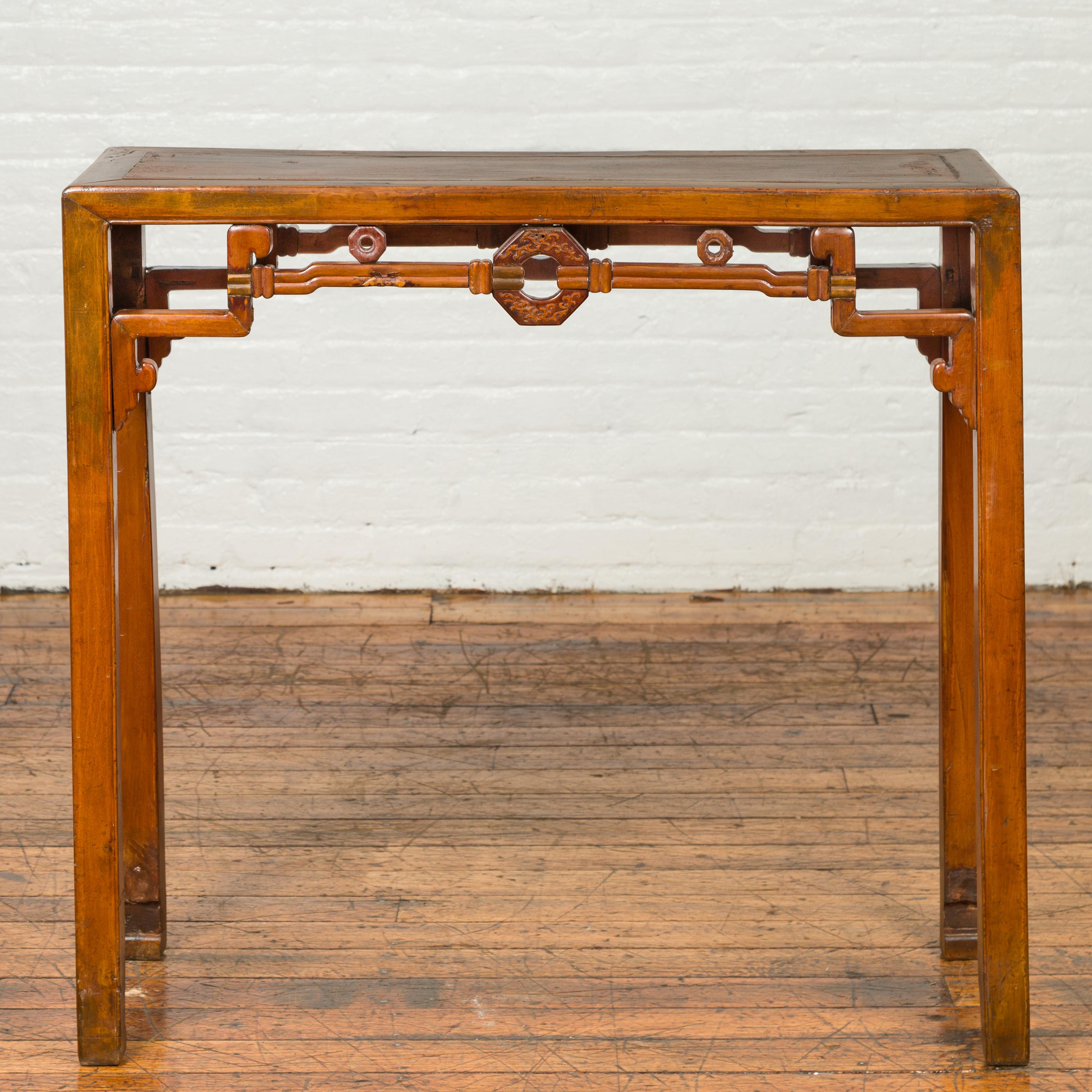 An antique Chinese wooden console table from the early 20th century, with coin patterns and horse-hoofed legs. Charming us with its clean lines and impeccable design, this antique Chinese altar console table features a rectangular top with central