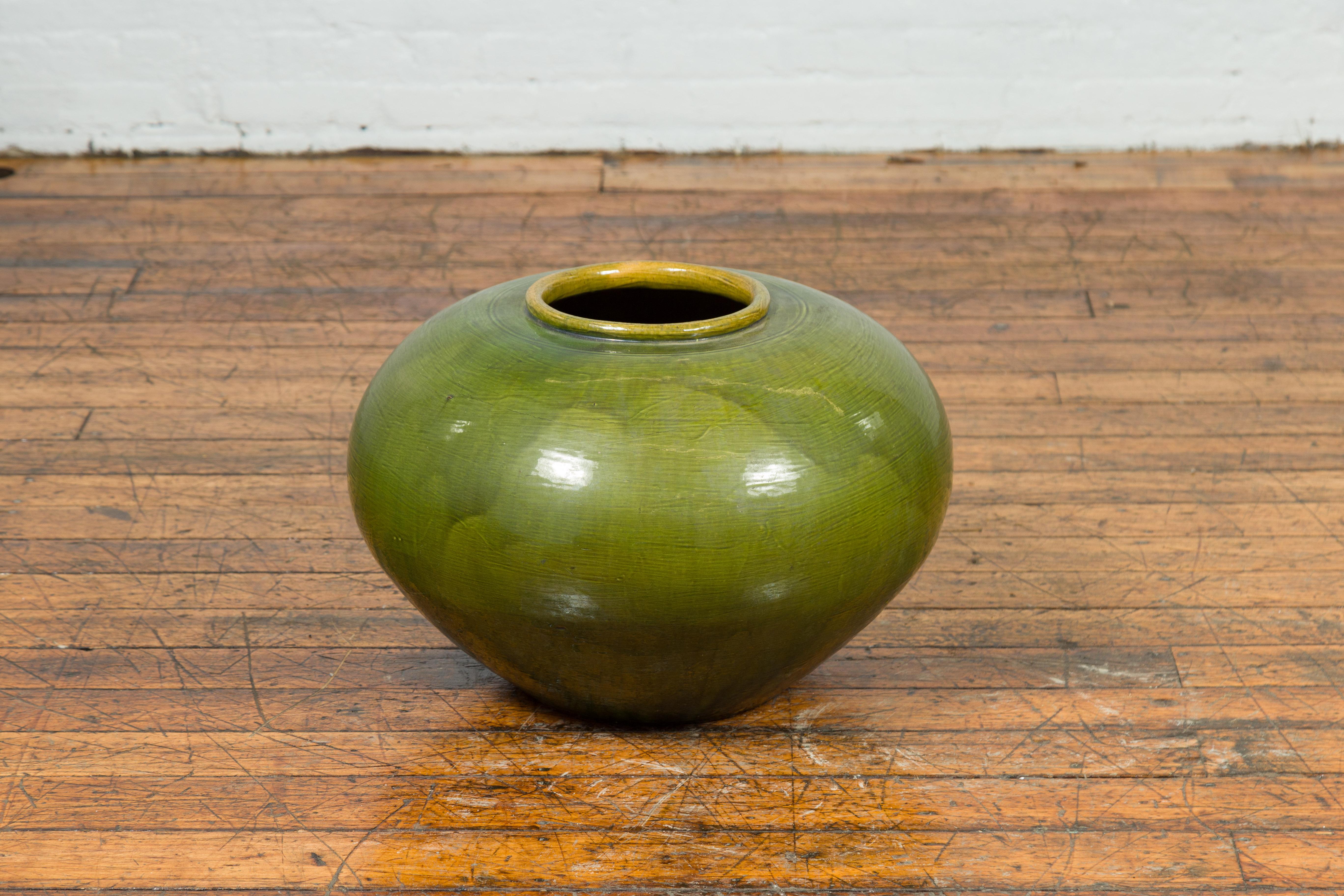 A Chinese contemporary olive green round urn with porcelain glaze. Created in China, this circular urn features a small lip topping a generous round body. Adorned with an olive green glaze with darker accents, this contemporary urn will bring a