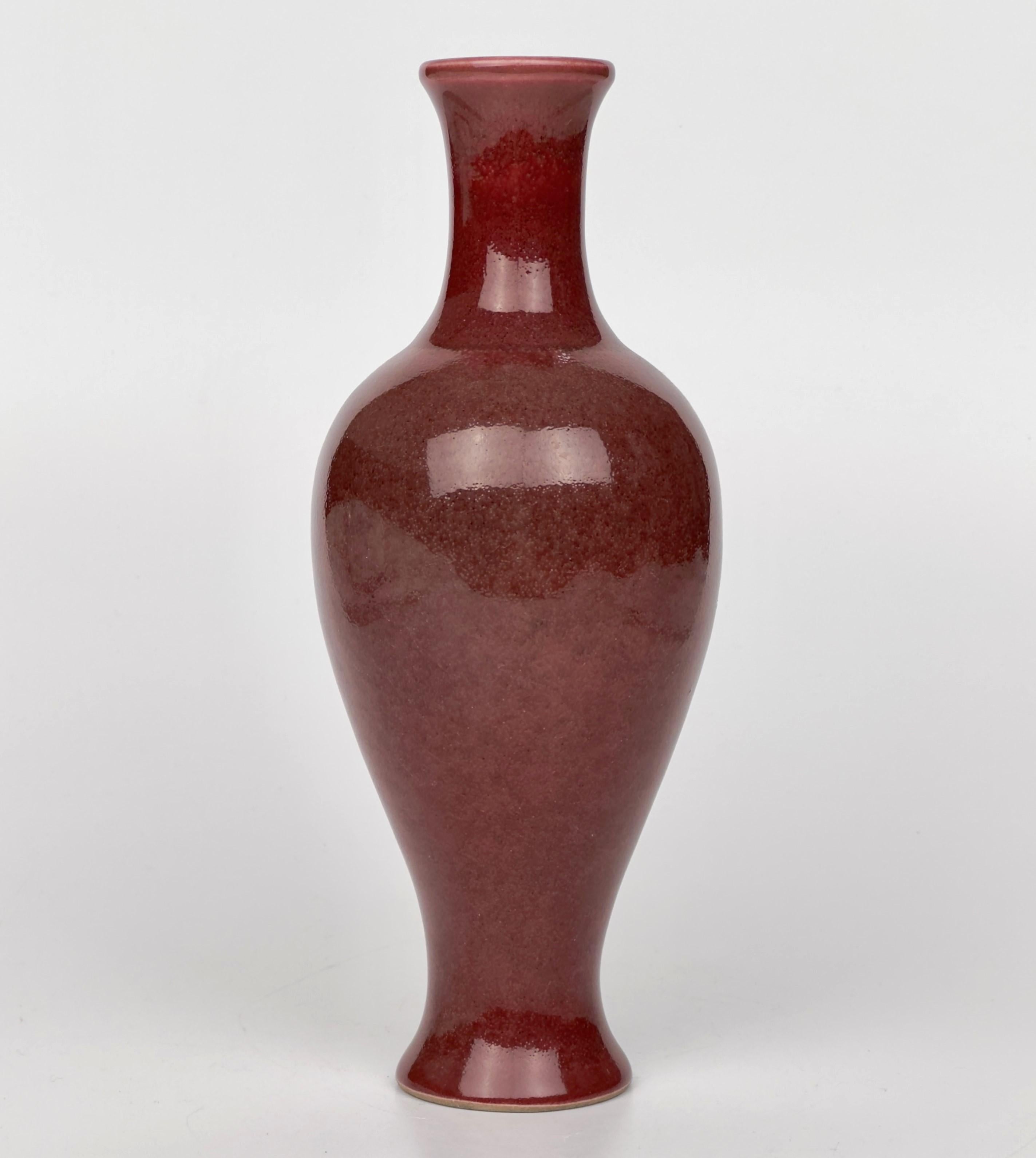 Qing Dynasty, Guangxu mark and of the period. The vase features a classic shape with a long, smooth body and a narrow opening. It is coated with a glossy, crimson glaze, often referred to as 'coral red', uniformly applied across its surface. It is