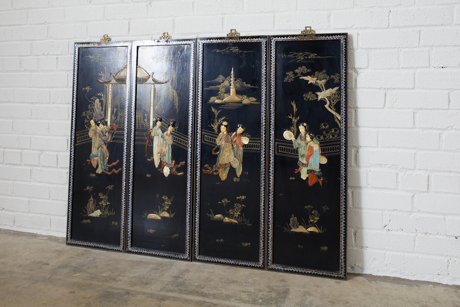 Set of 4 Chinese black lacquer coromandel style panels featuring colorful hardstone decoration. Each depicting 2 beauties in the garden with pagodas and foliate finished gilt. Each wood panel is suspended from a brass metal hanger mount with an open