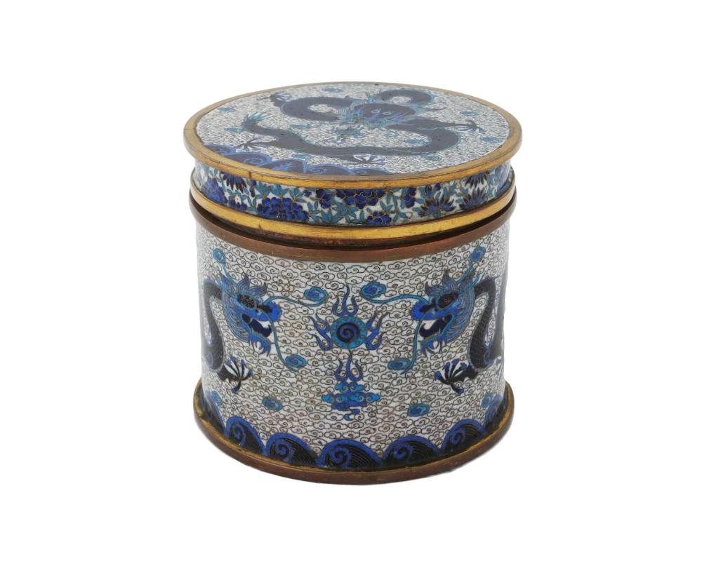 A Chinese covered enamel box. The exterior of the ware is adorned with a polychrome design depicting dragons over waves surrounded by a cloud motif made in the Cloisonne technique. The cover of the box is decorated with an image of a dragon flying