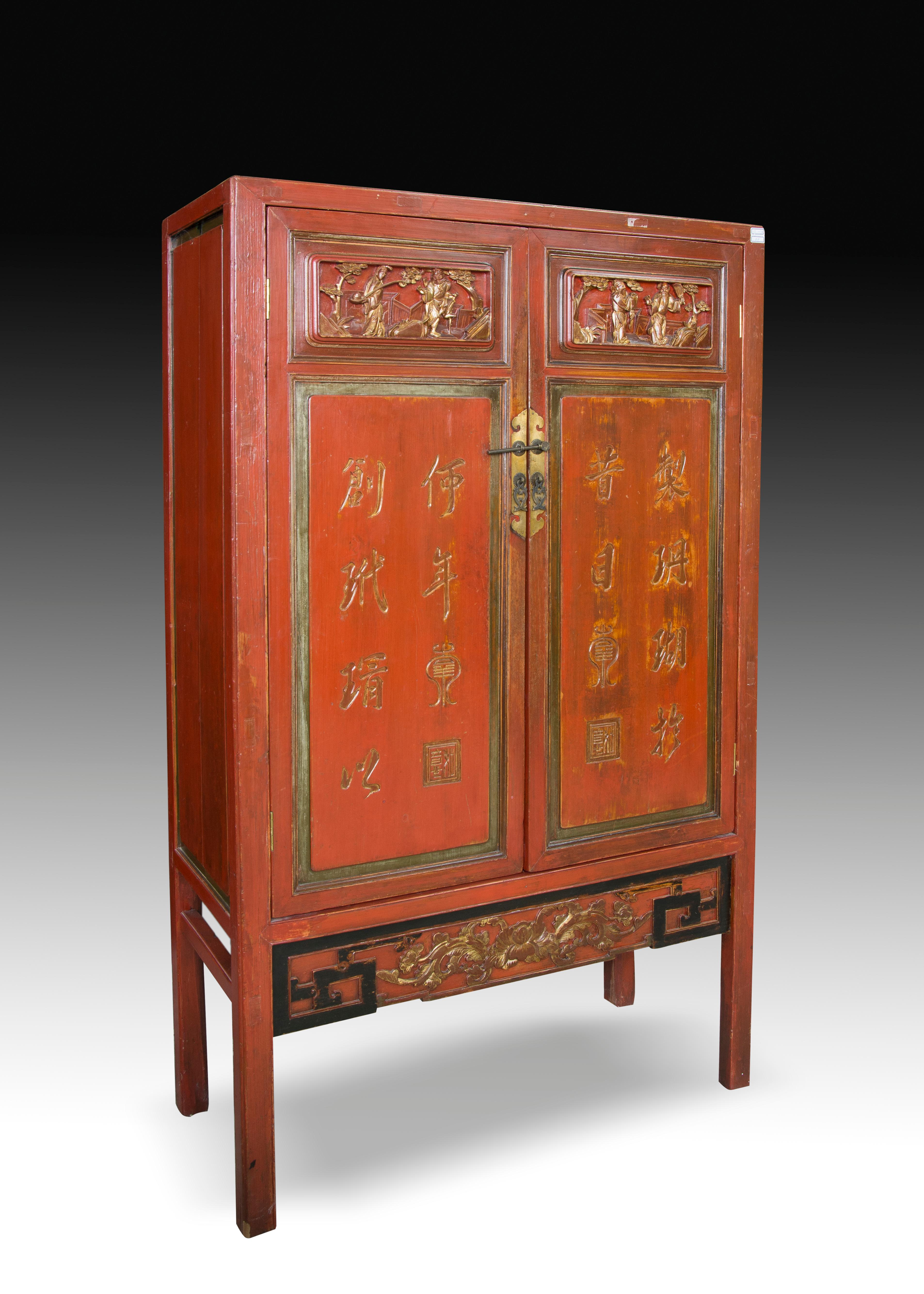 Tall wardrobe with two doors to the front decorated with Chinese characters and figurative scenes on them, and with a band below with geometric patterns in black enhancing a floral composition. Inside, there are three shelves and two drawers with
