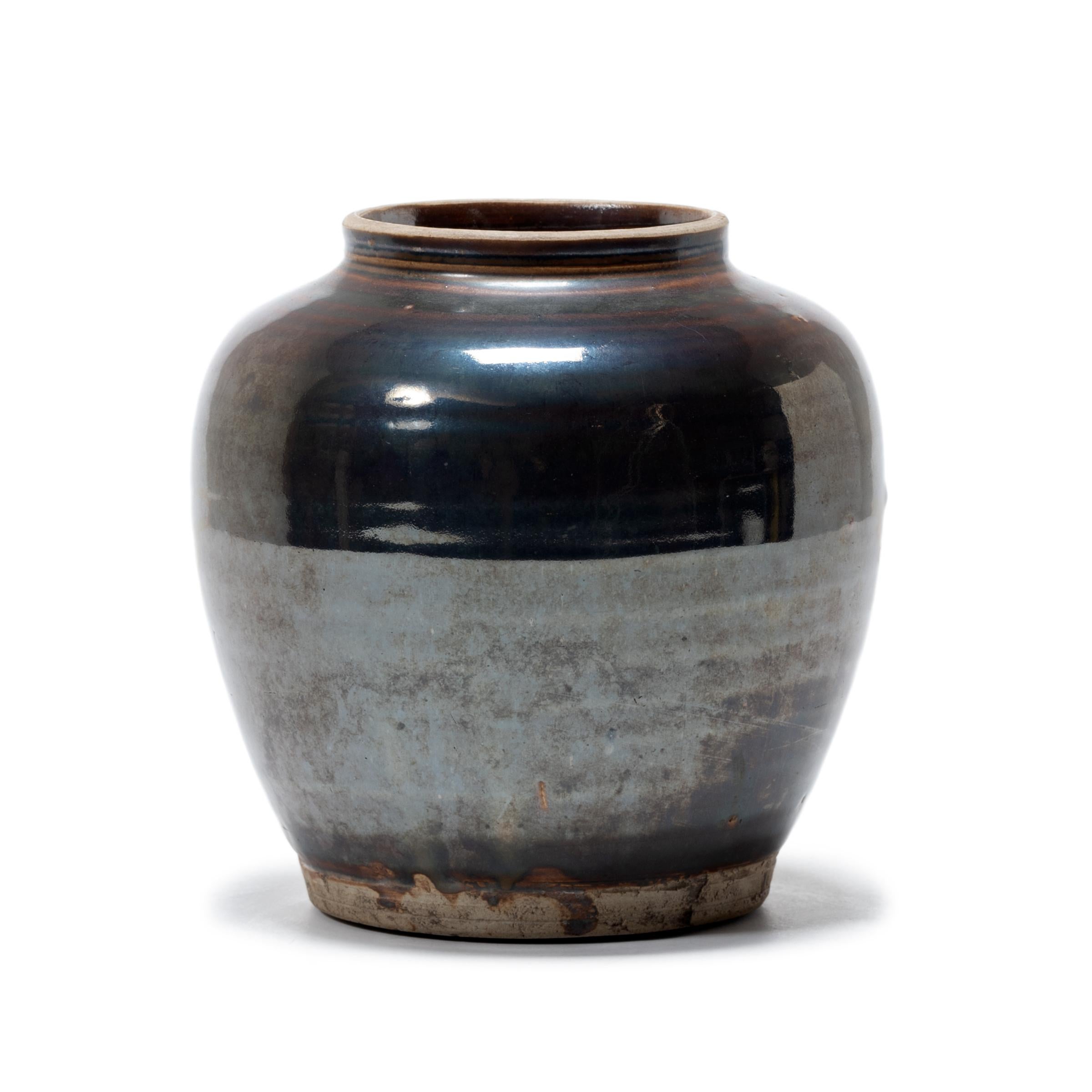 A shimmering brown glaze clings to the textured surface of this petite jar, lingering on subtle ridges ringing the jar's gradual tapered form. Crafted in the late 19th century, the wide-mouth jar was once used to store food in a Qing-dynasty