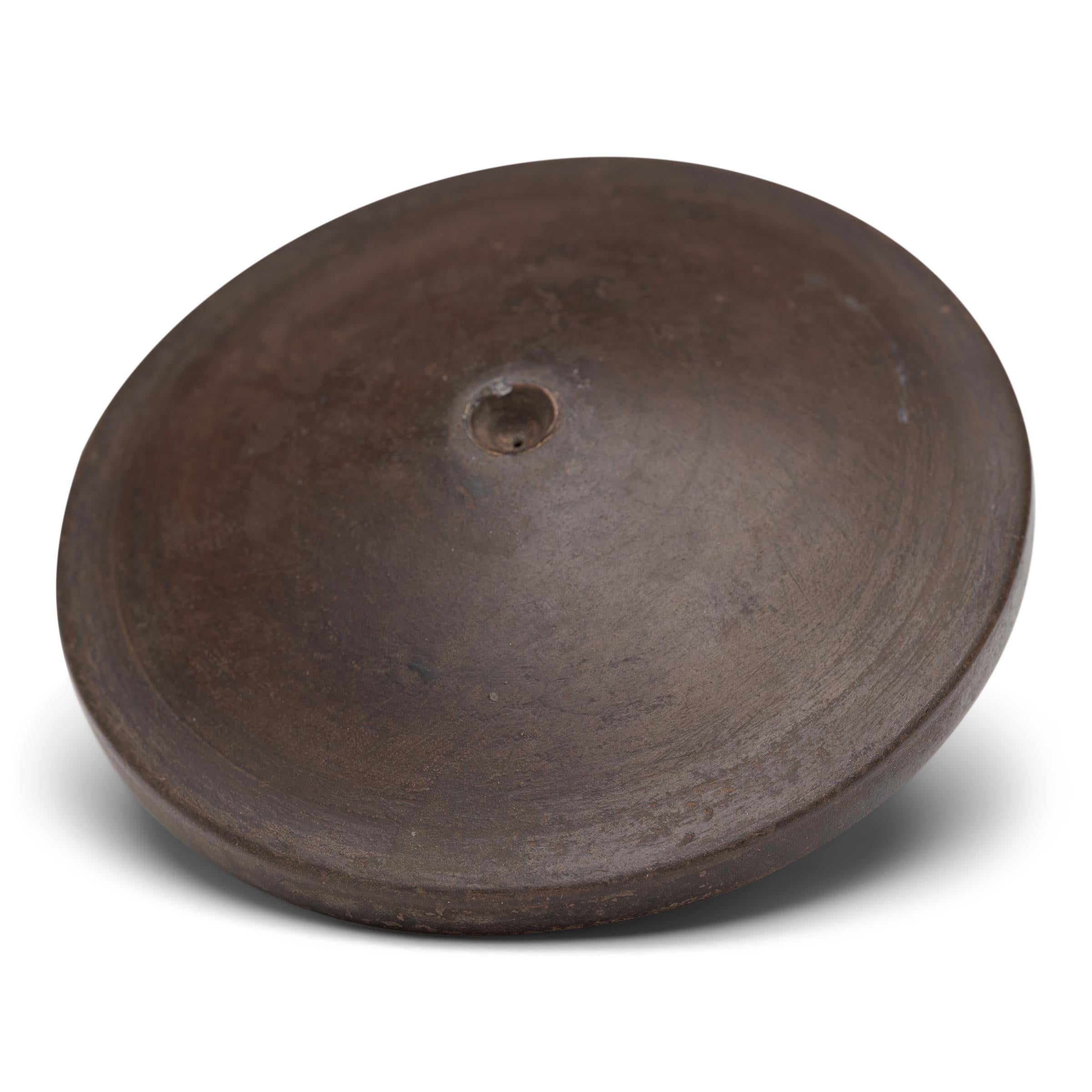 This unusual object is a 19th century opium pipe bowl, beautifully sculpted of dark clay to a thin, discus form and fitted with a copper collar. Minimal and refined, the pipe bowl is decorated only by a geometric meander etched into the underside