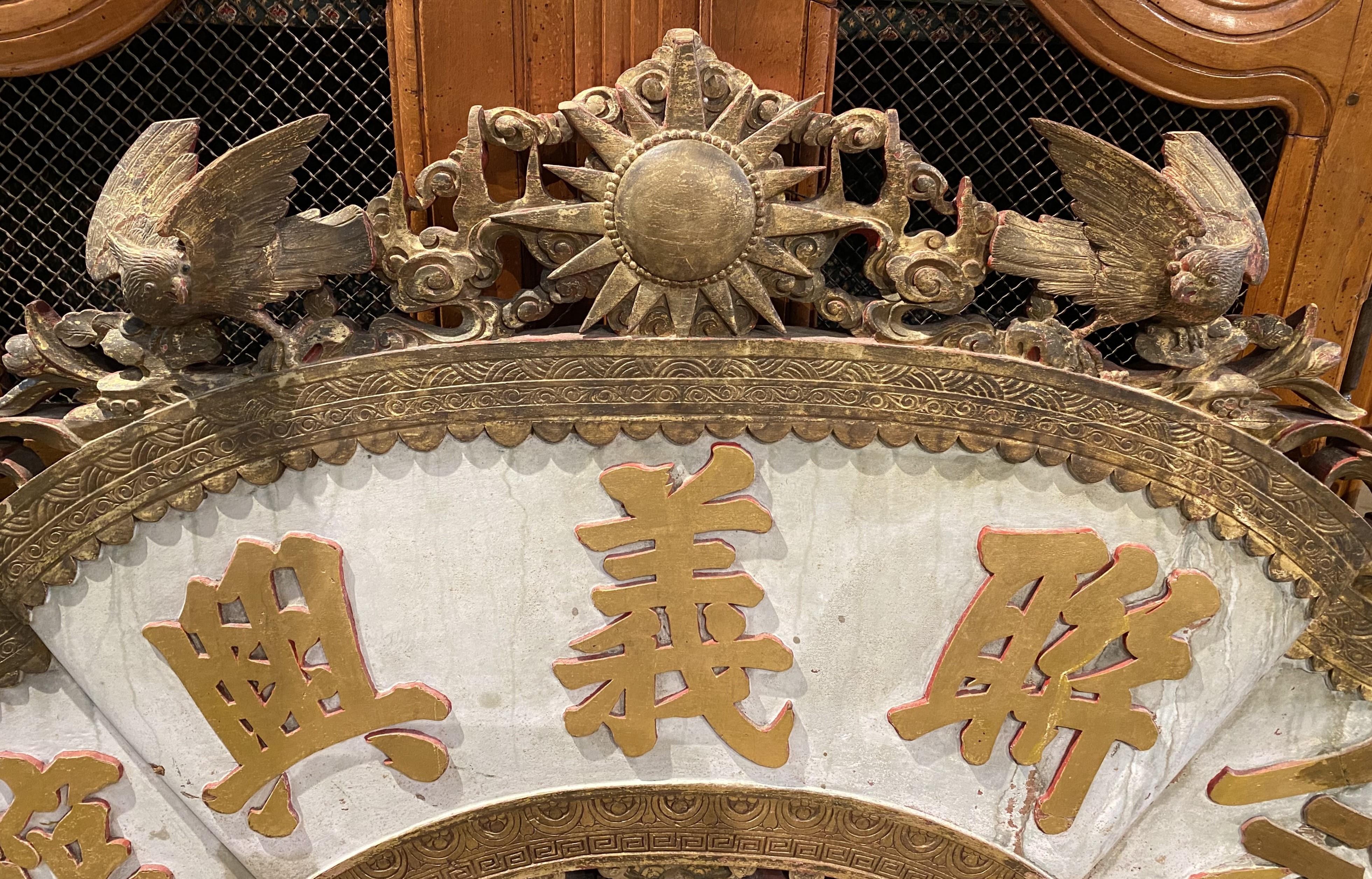 A fine Chinese decorative carved wooden architectural pediment, most likely from a temple, its crest featuring a gilt carved center star flanked by pierce carved birds, flowers, scrollwork, and dragons. Large Chinese gilt symbols appear across the