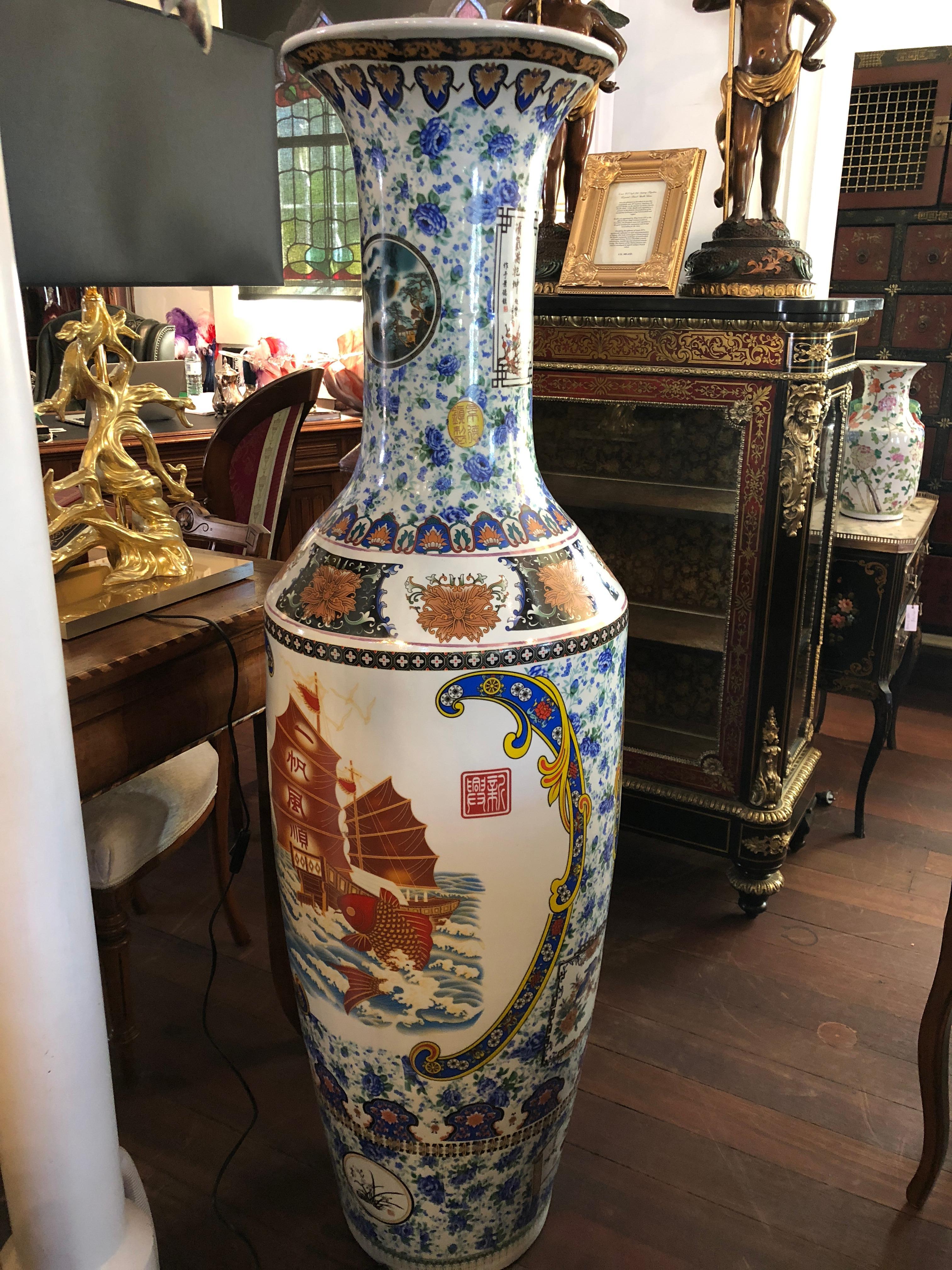 This grand Chinese floor vase is adorned with beautiful, hand painted depictions of flowers and traditional Chinese symbols such as dragon boats and koi fish. Toward the top lip of this grand vase, there are small panels of Chinese calligraphy,