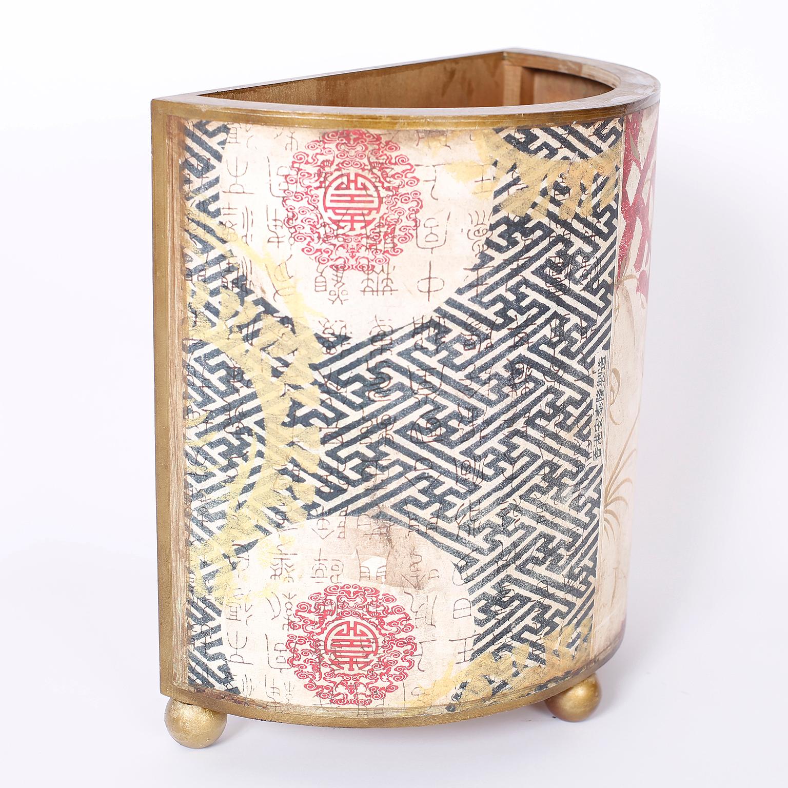 Demilune wastepaper basket or trash can decorated with lithographic Chinese characters against geometric and floral designs set on ball feet.