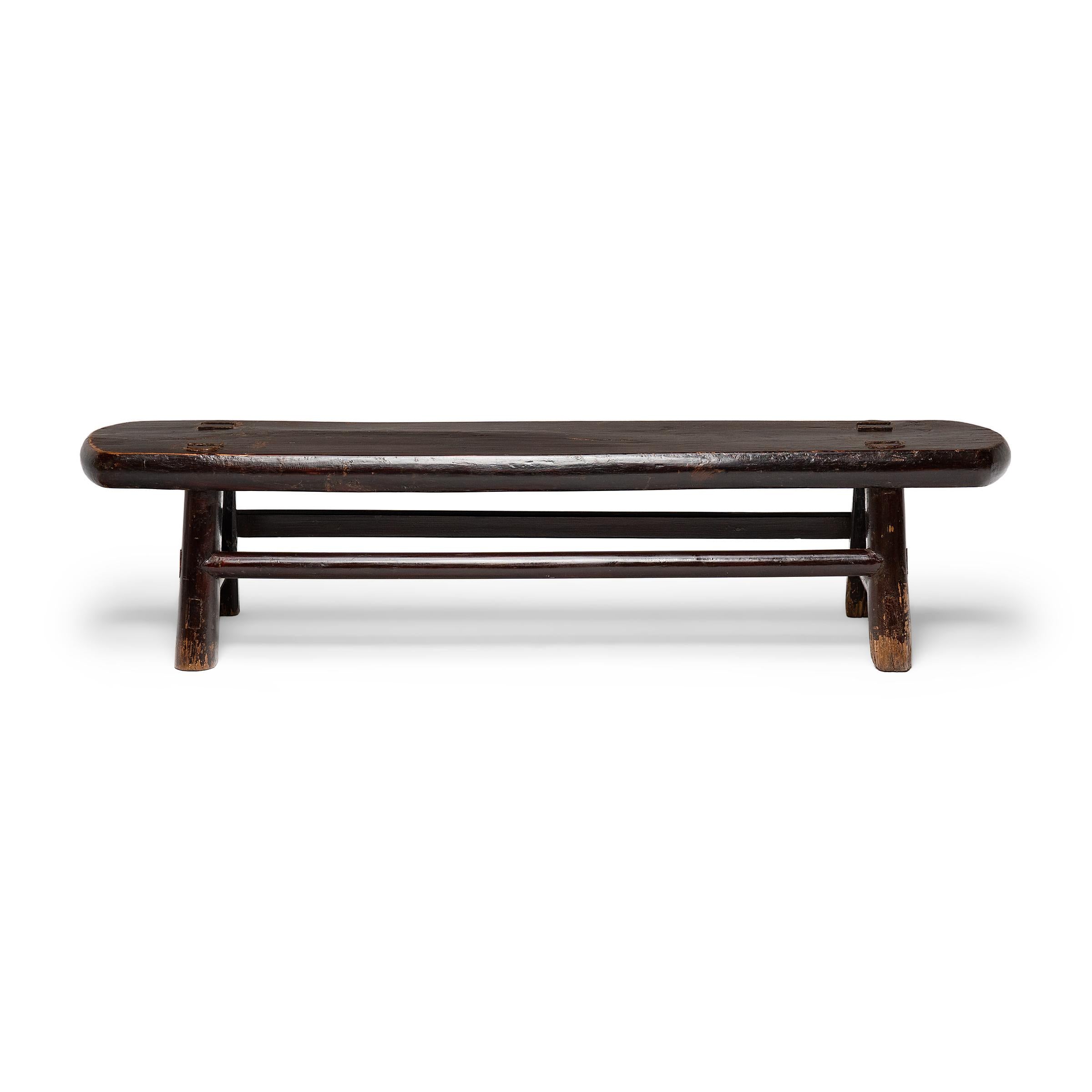 A low daybed step from the mid-19th century, featuring an elongated plank top with rounded ends and short splayed legs linked with straight stretchers. Crafted with mortise-and-tenon joinery, without the use of nails or screws, the legs connect to