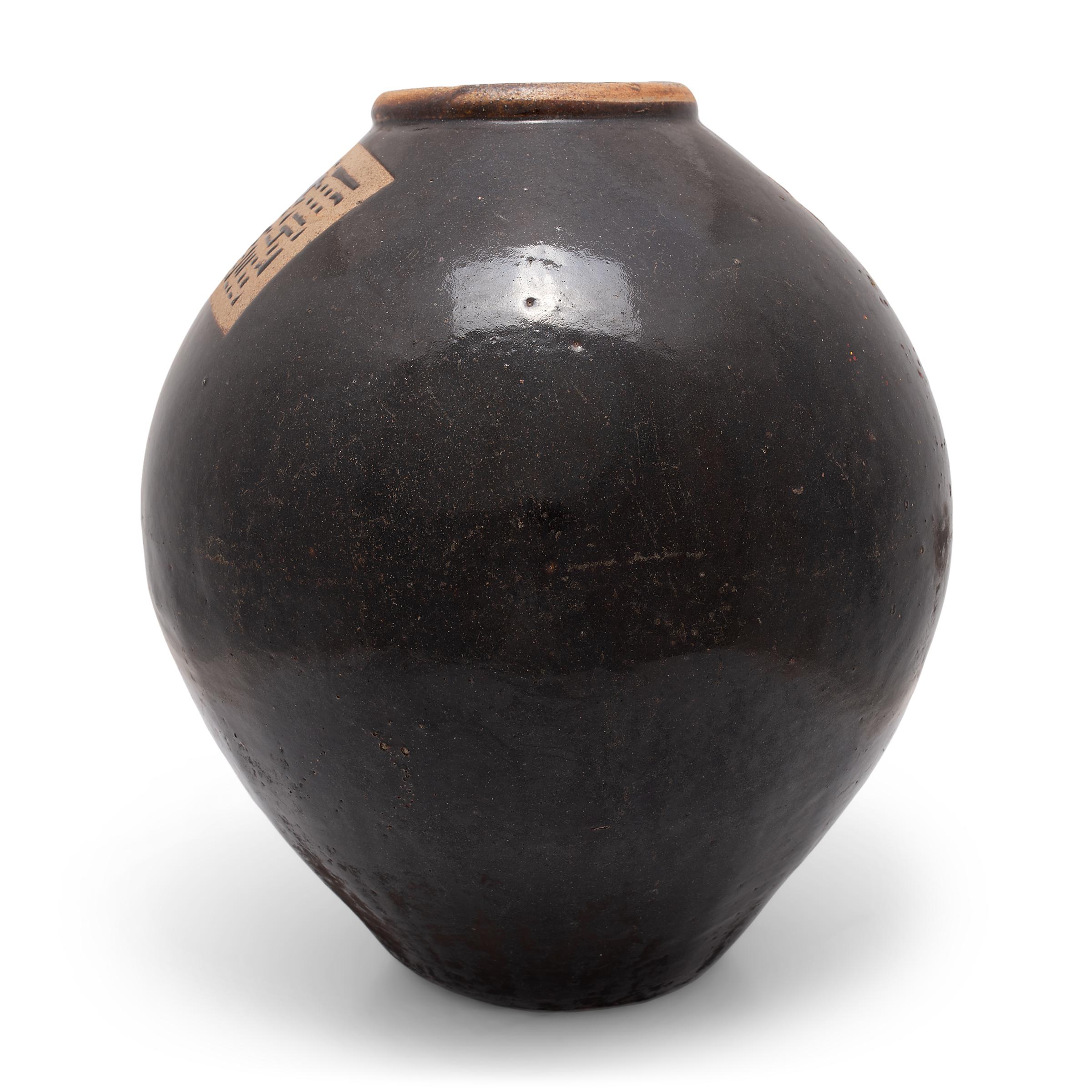 This early 20th-century ceramic jar is formed in a traditional shape meant for storing wine and spirits made from rice and grains. Known as cheng, these jars are defined by having a wide body with dramatically restricted neck and base, and were also