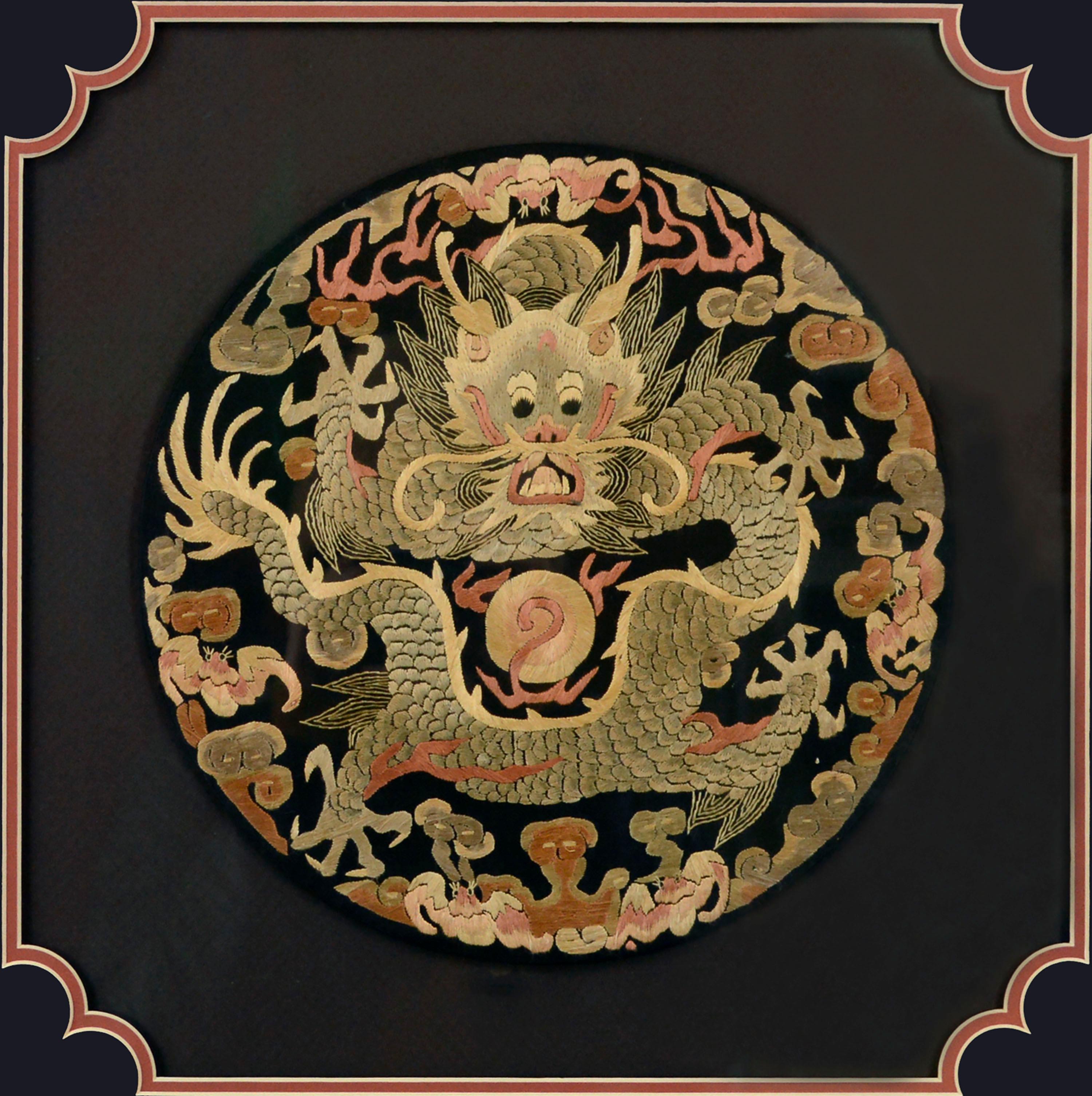 Late 19th century Chinese silk embroidery rank badge textile, with a finely detailed dragon along with other various symbols embroidered with light yellow, tan, rust orange, and light red thread on a black background. The dragon's claws are each